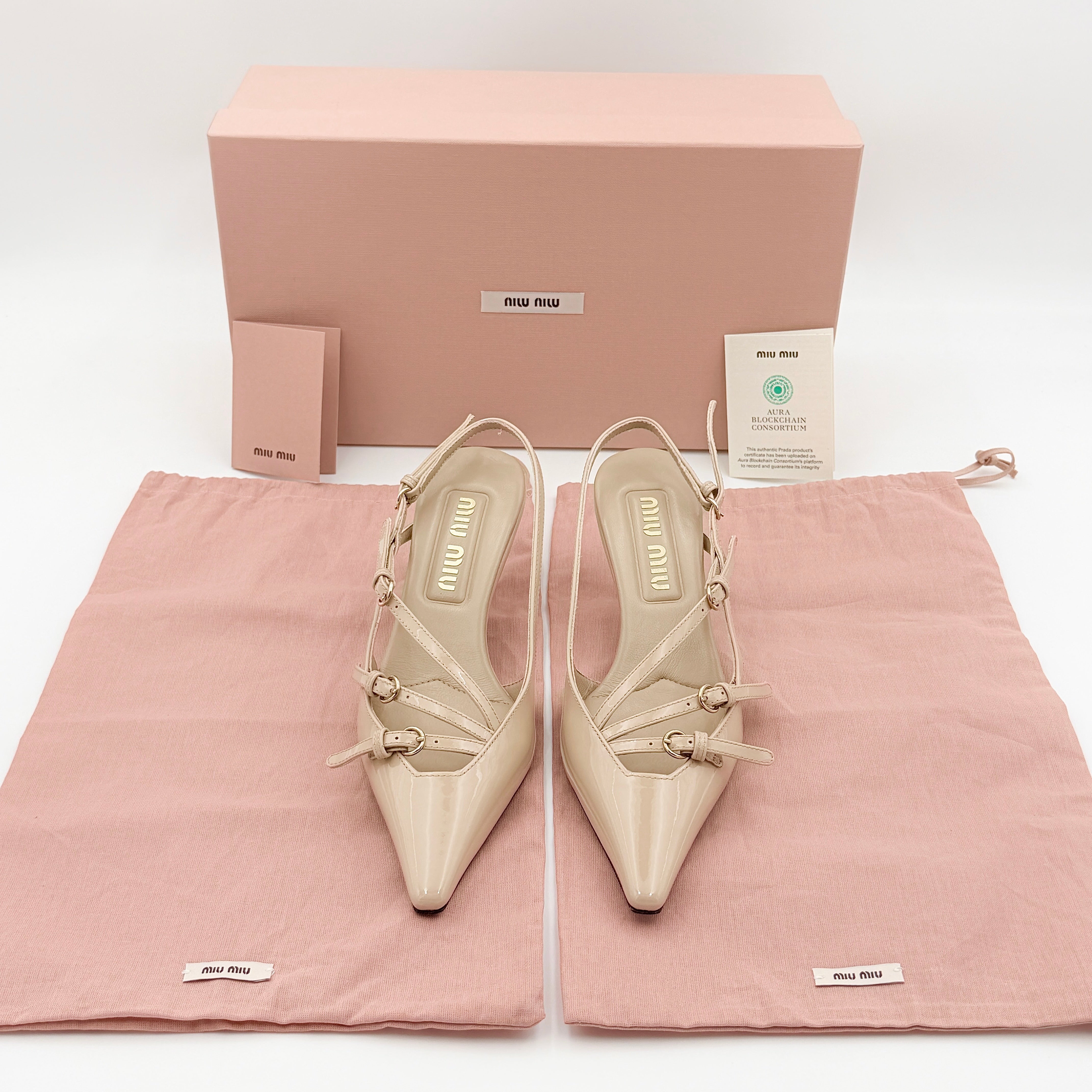 A pair of Miu Miu beige patent leather slingback pumps with pointed toes and gold-tone buckles displayed on a white background.