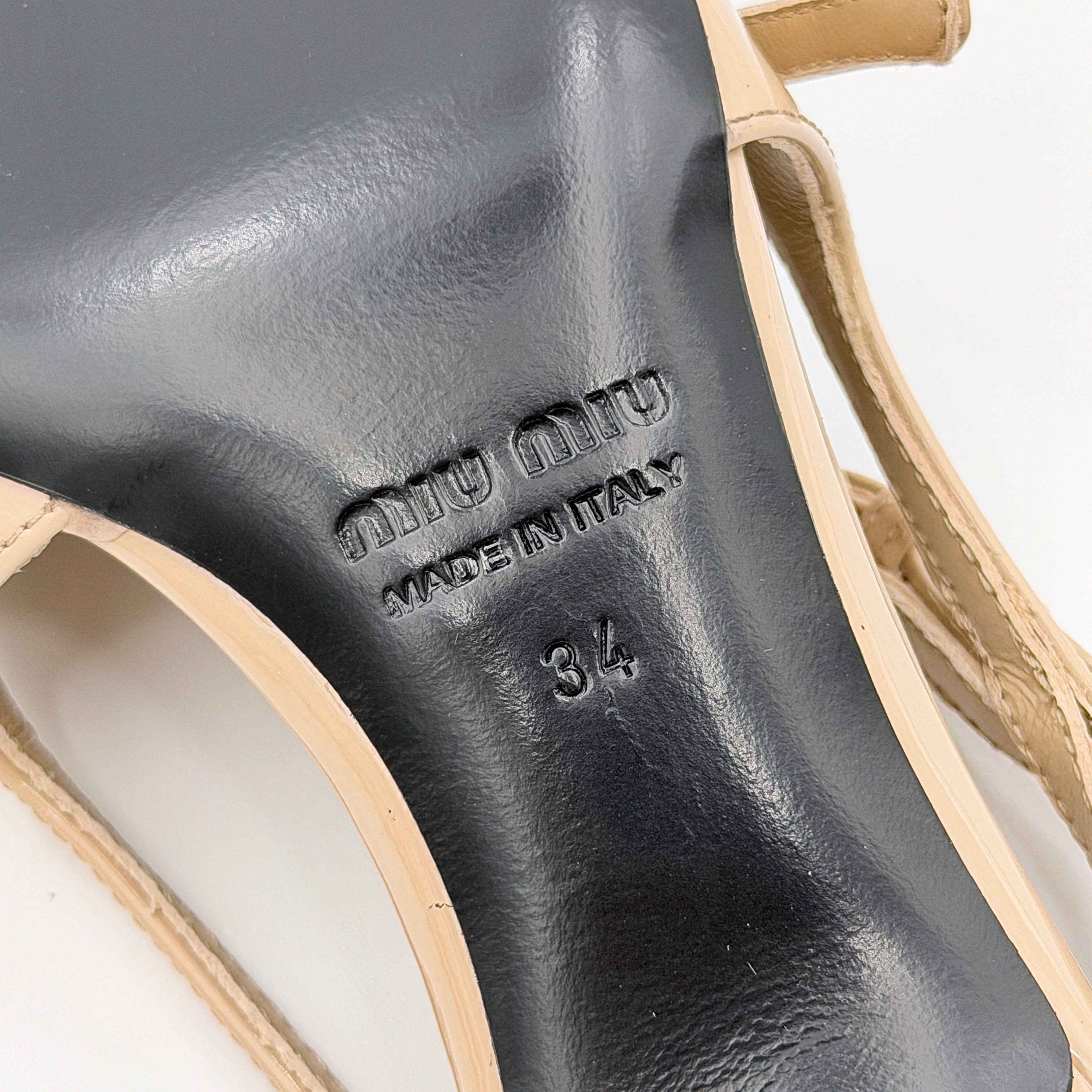 A pair of Miu Miu beige patent leather slingback pumps with pointed toes and gold-tone buckles displayed on a white background.