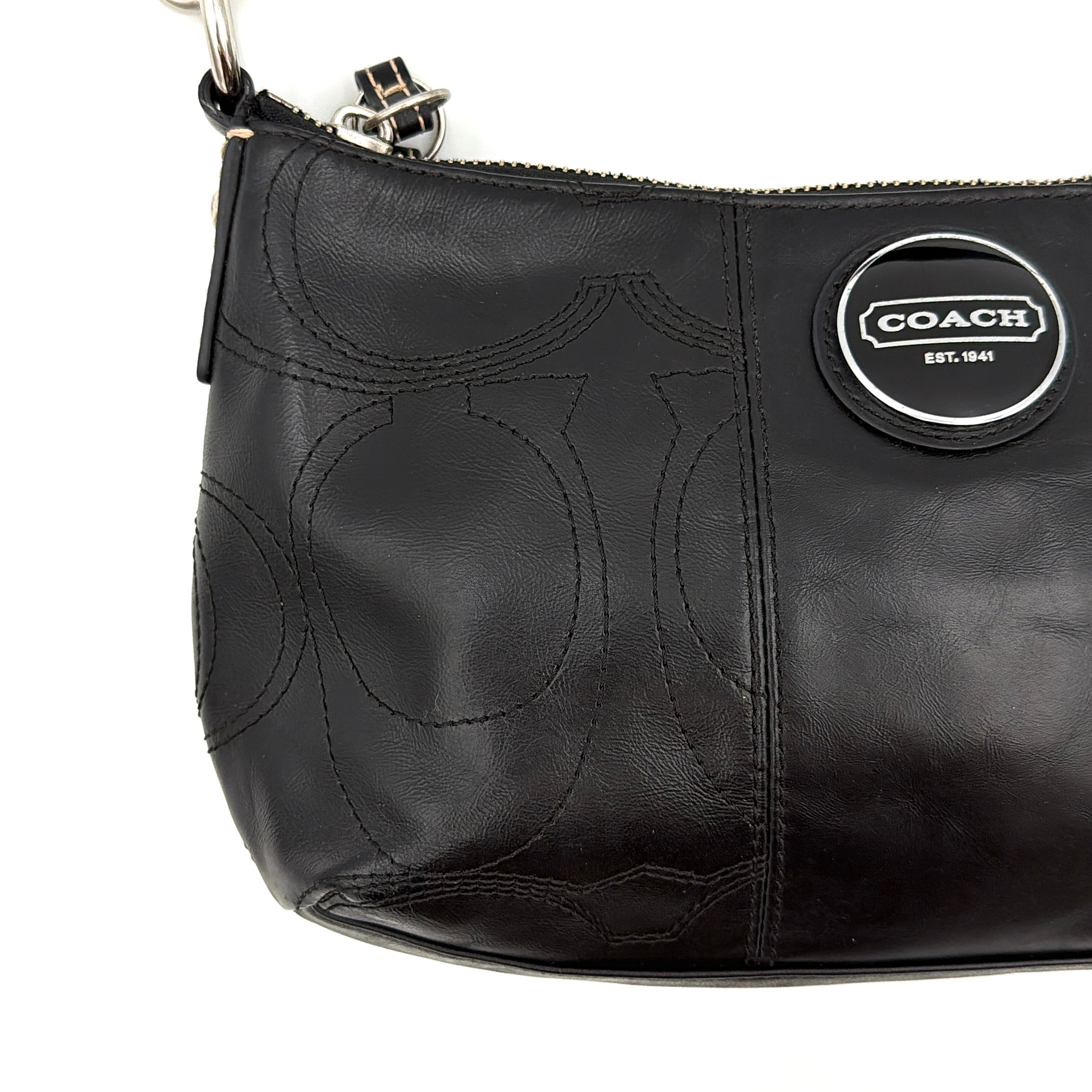 Coach black leather shoulder bag with signature embossed pattern and silver hardware, shown with attached logo tag and short leather strap.