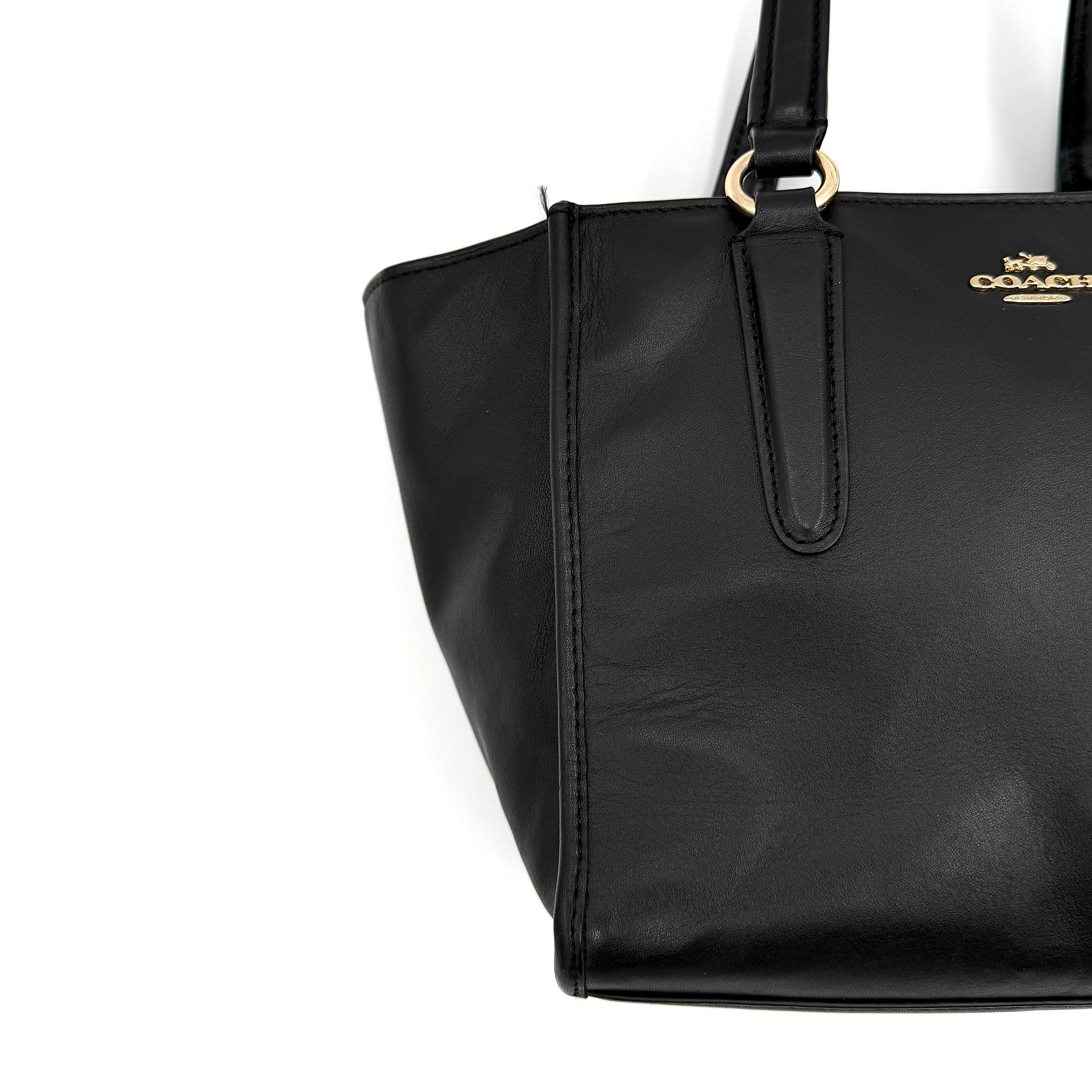 The Coach 2Way Mini Crosby Carryall Handbag in smooth black leather with gold-tone hardware, top handles, and detachable strap displayed alongside.