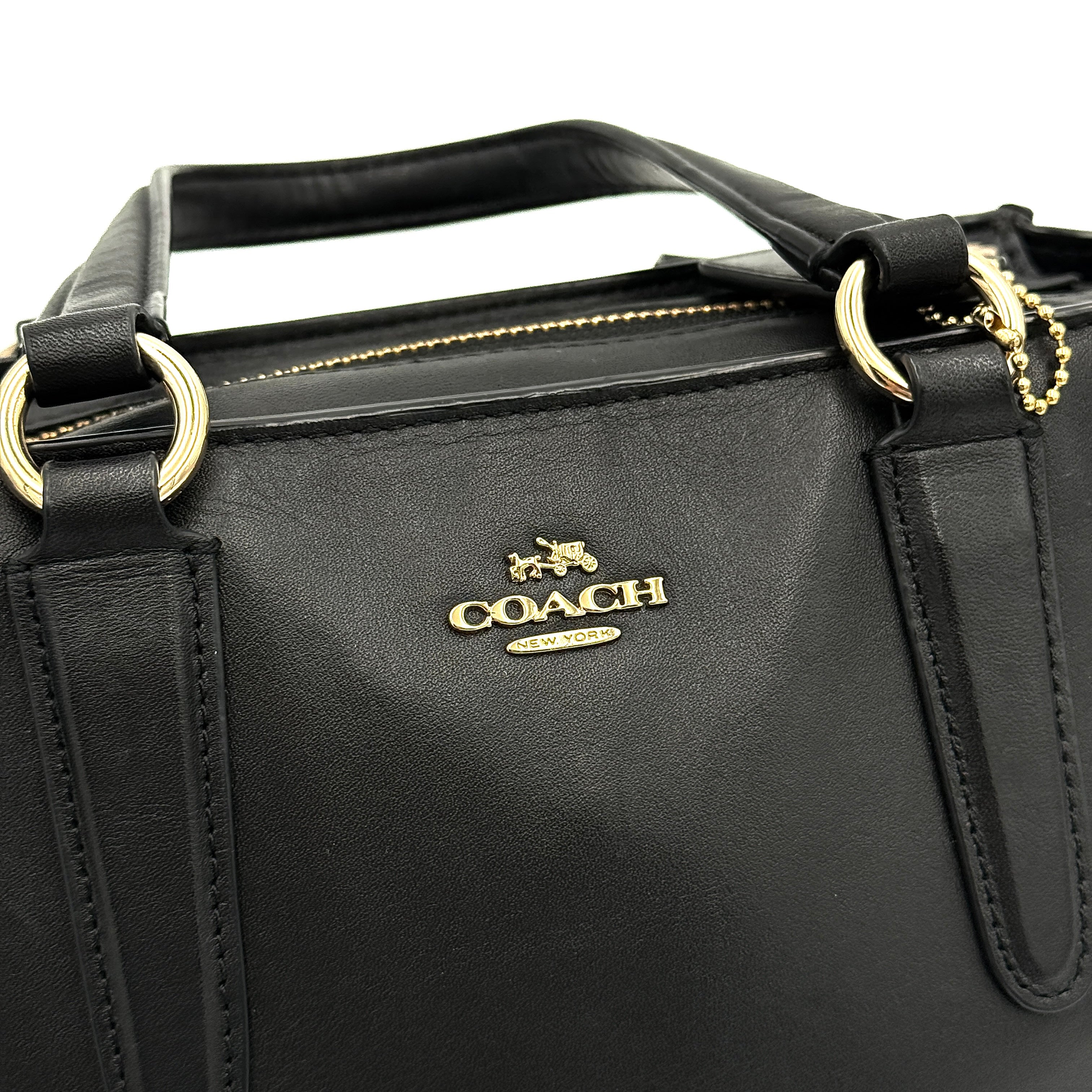 The Coach 2Way Mini Crosby Carryall Handbag in smooth black leather with gold-tone hardware, top handles, and detachable strap displayed alongside.