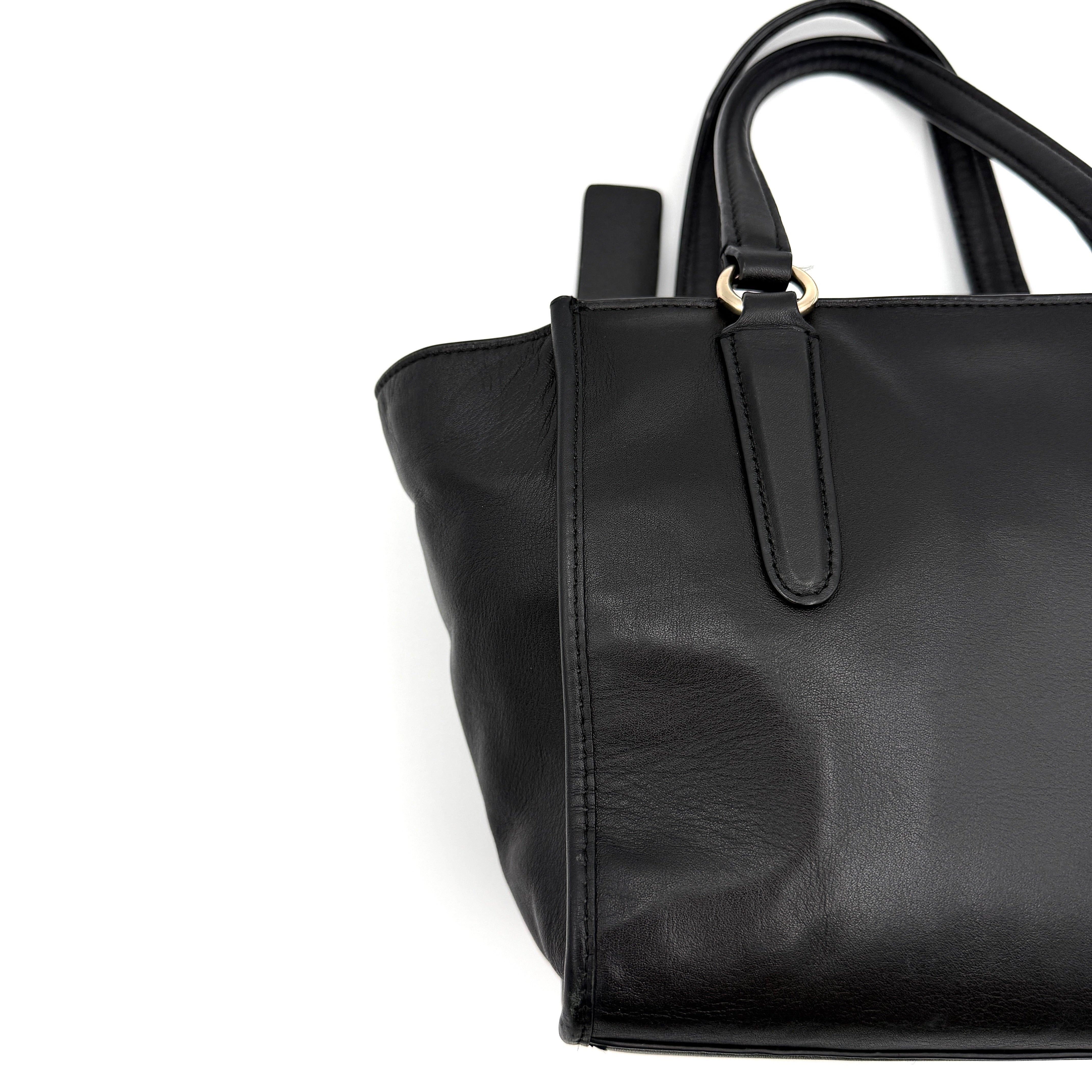 The Coach 2Way Mini Crosby Carryall Handbag in smooth black leather with gold-tone hardware, top handles, and detachable strap displayed alongside.
