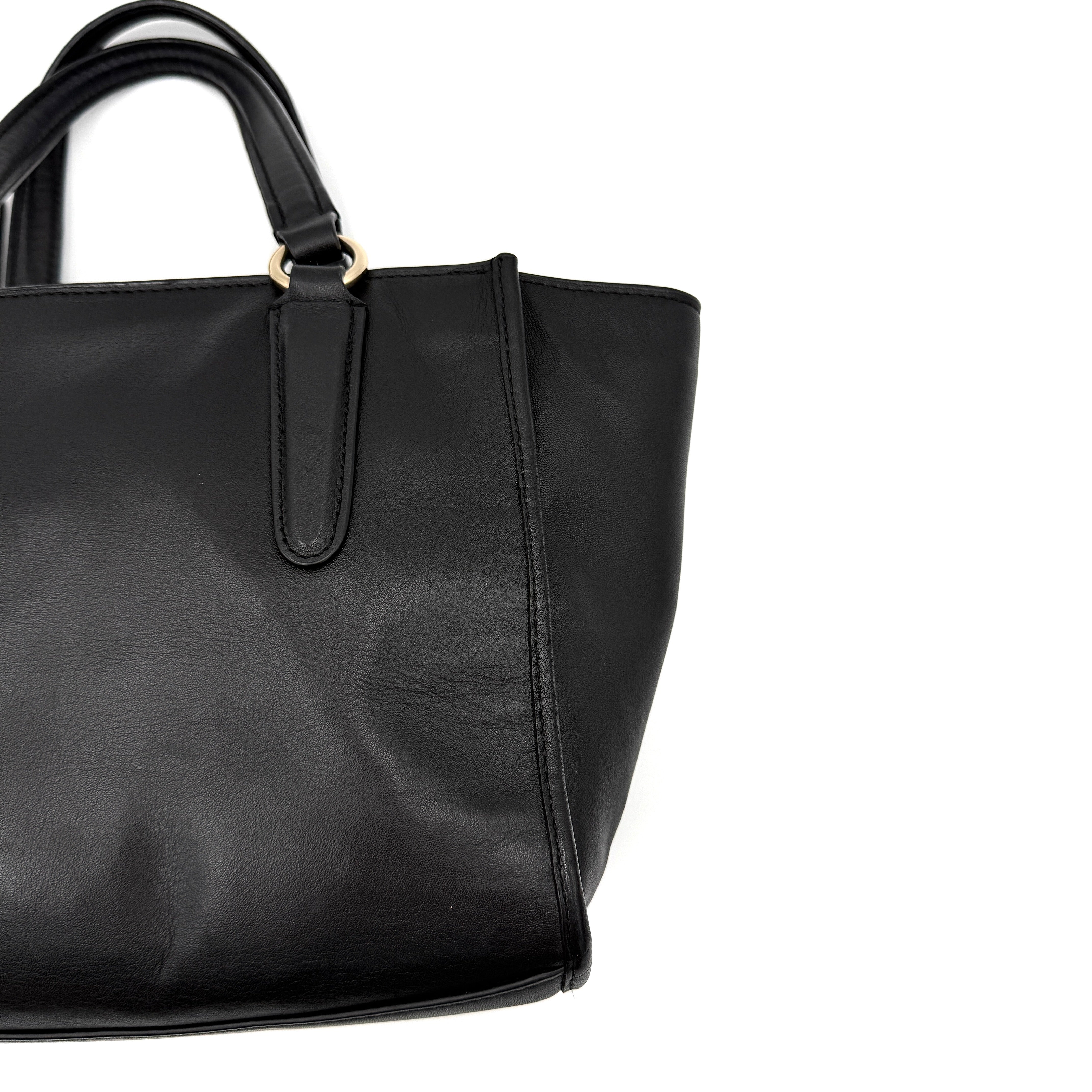 The Coach 2Way Mini Crosby Carryall Handbag in smooth black leather with gold-tone hardware, top handles, and detachable strap displayed alongside.