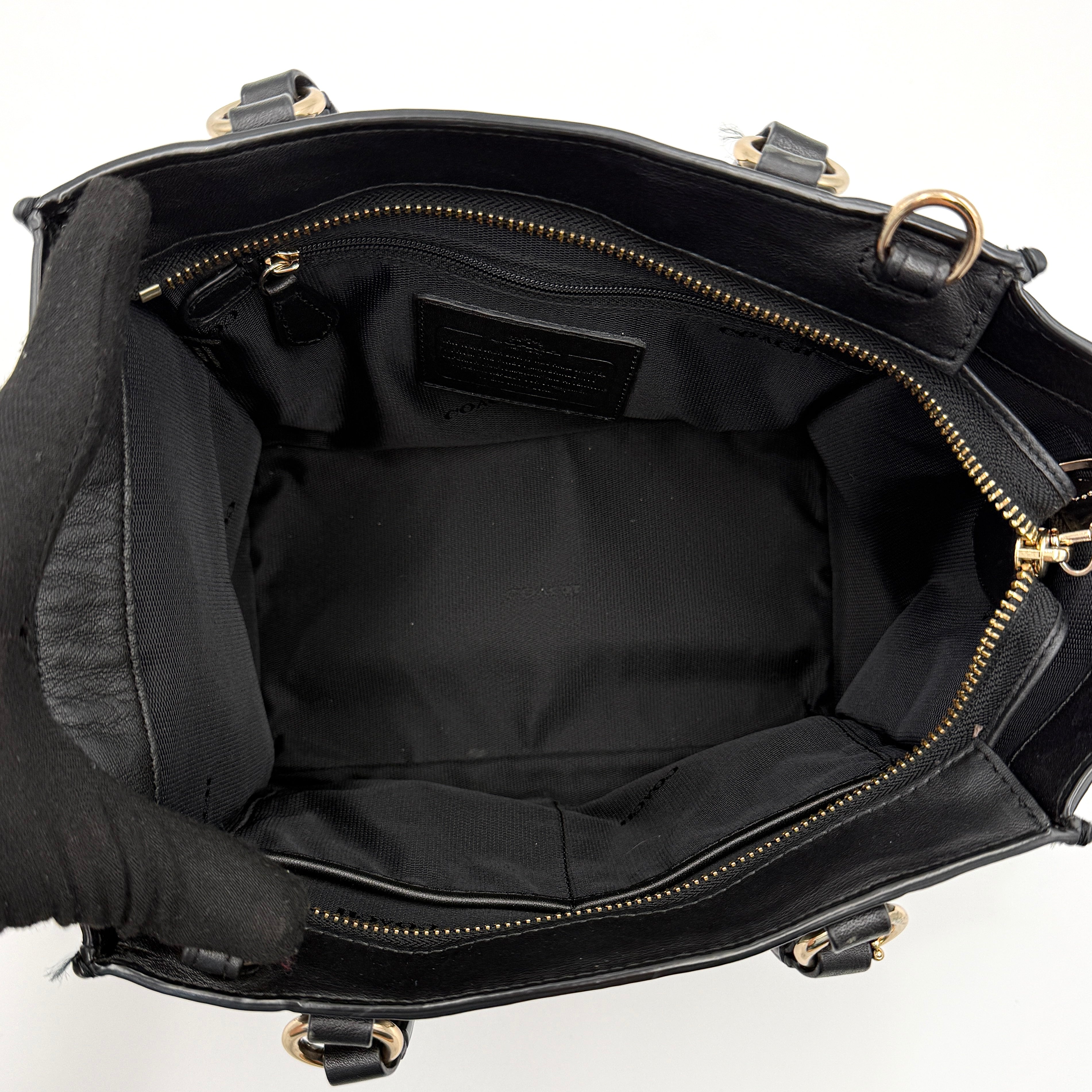 The Coach 2Way Mini Crosby Carryall Handbag in smooth black leather with gold-tone hardware, top handles, and detachable strap displayed alongside.
