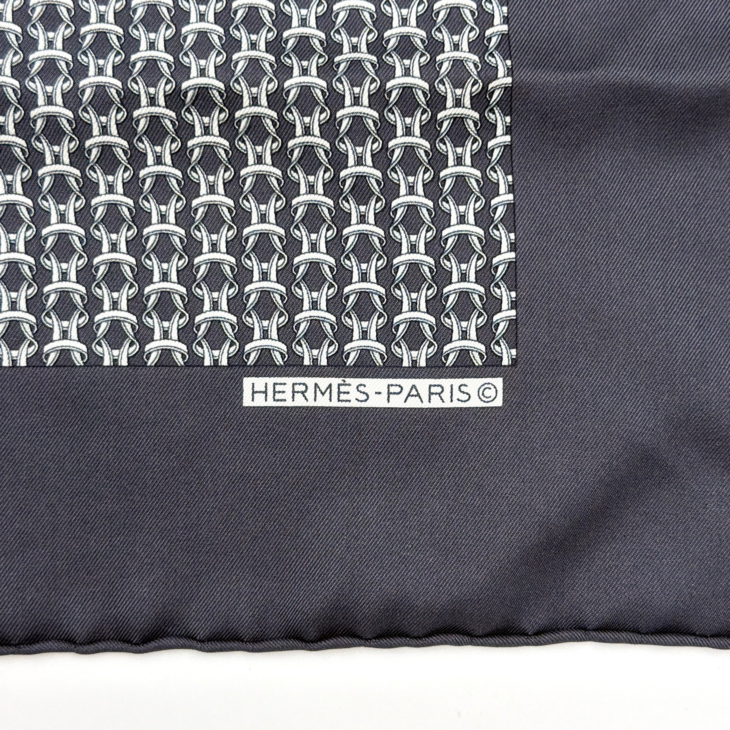 Hermès silk scarf in navy blue with a white chain link pattern and bold border, elegantly displayed flat.