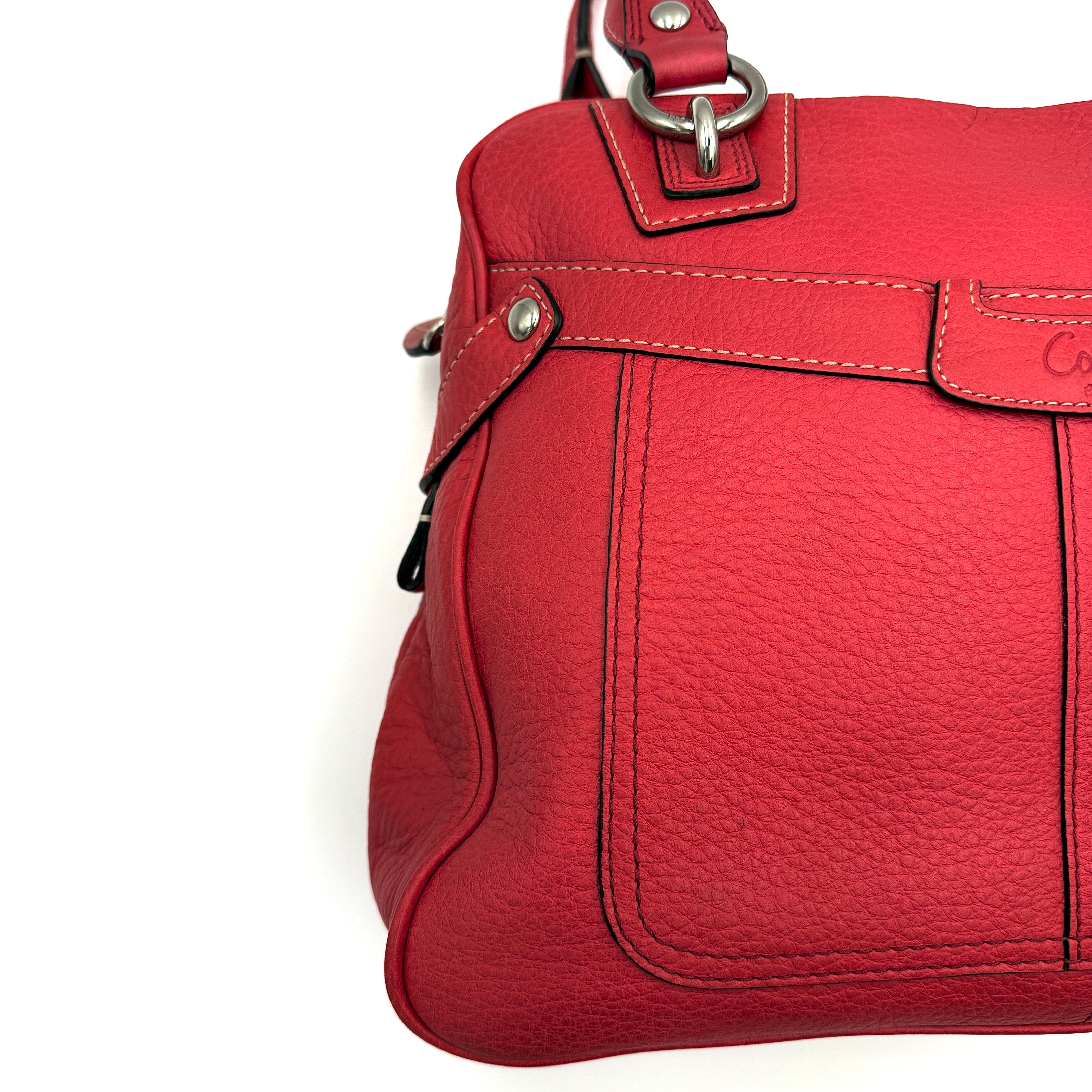 Coach red pebbled leather satchel with dual rolled handles, silver hardware, and structured silhouette.