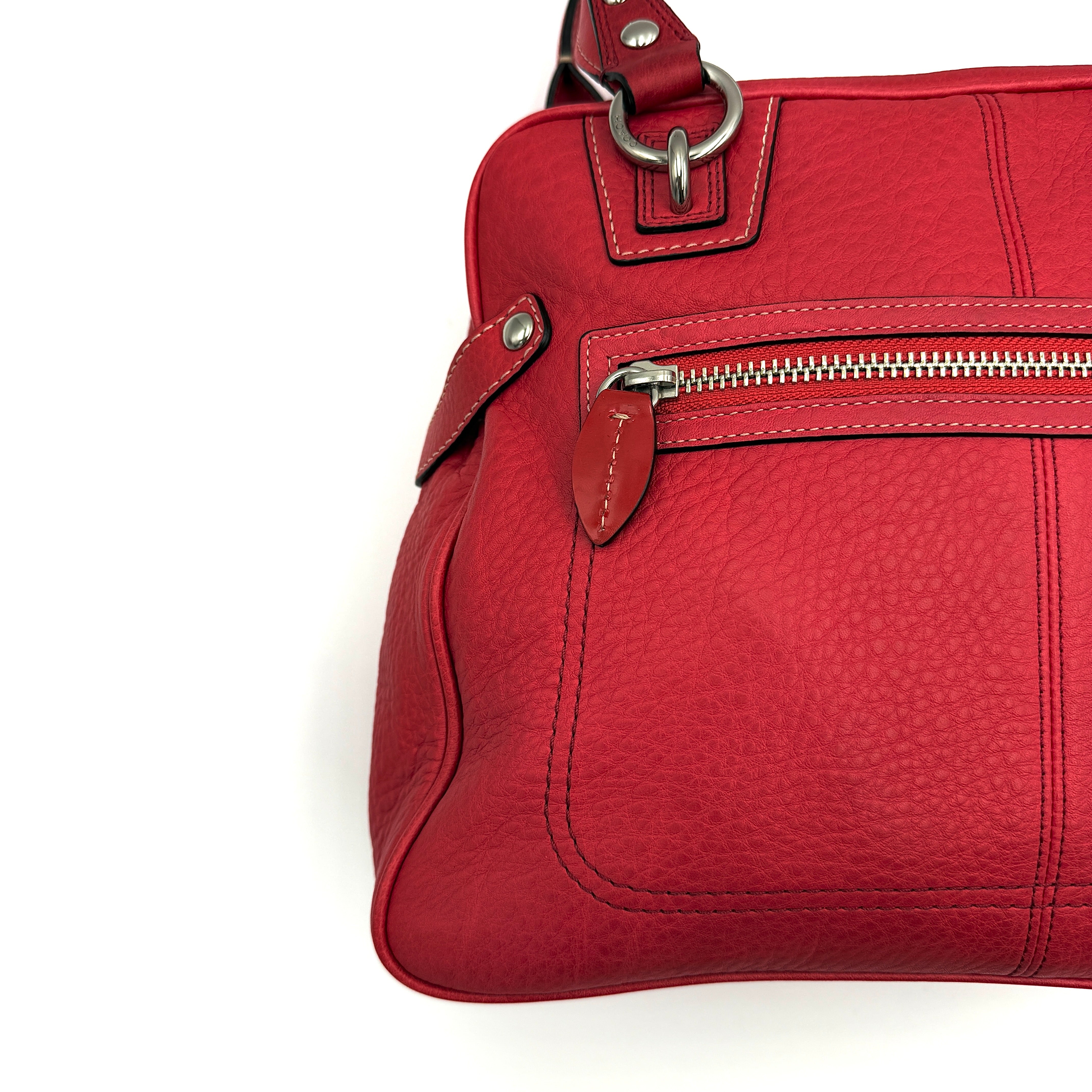 Coach red pebbled leather satchel with dual rolled handles, silver hardware, and structured silhouette.