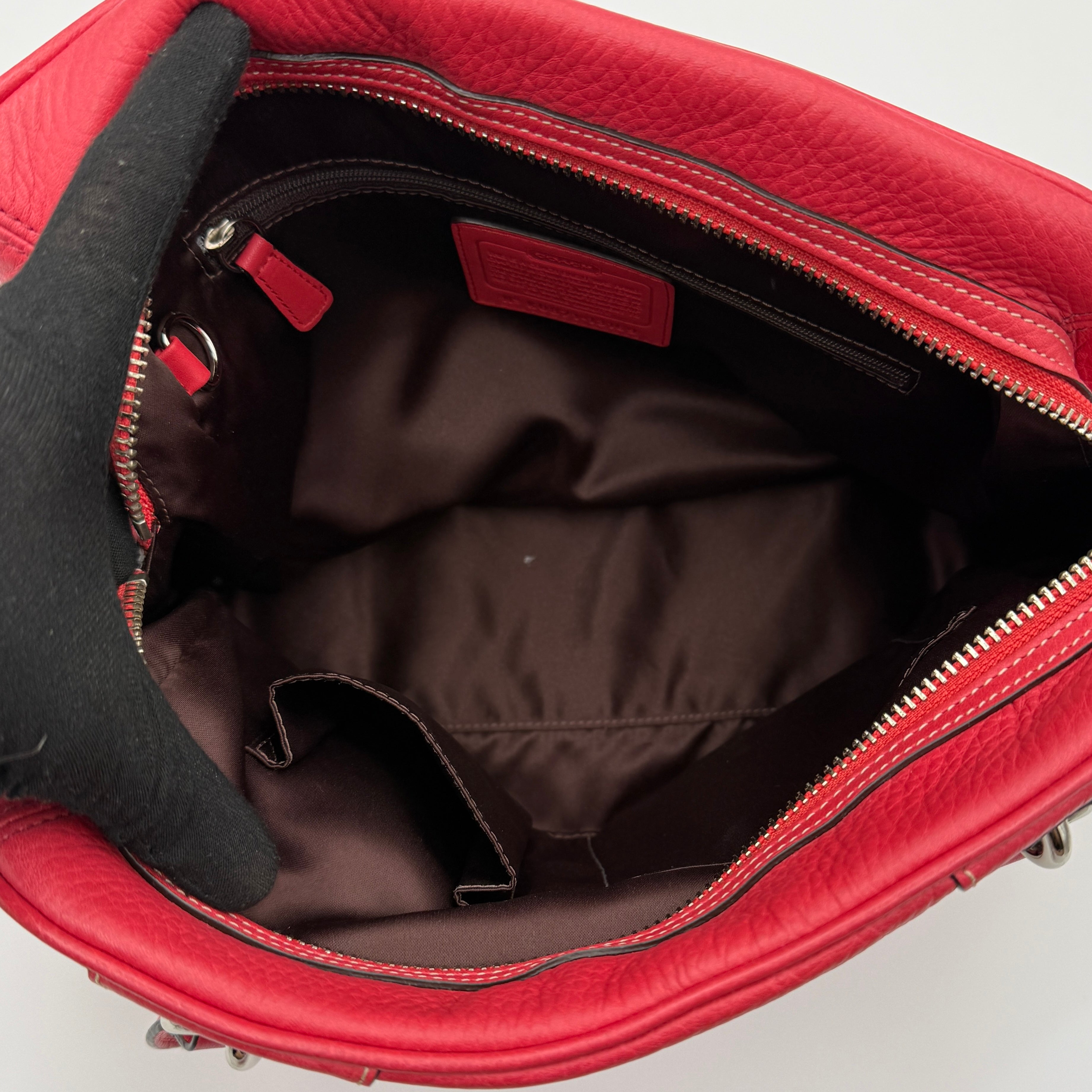 Coach red pebbled leather satchel with dual rolled handles, silver hardware, and structured silhouette.