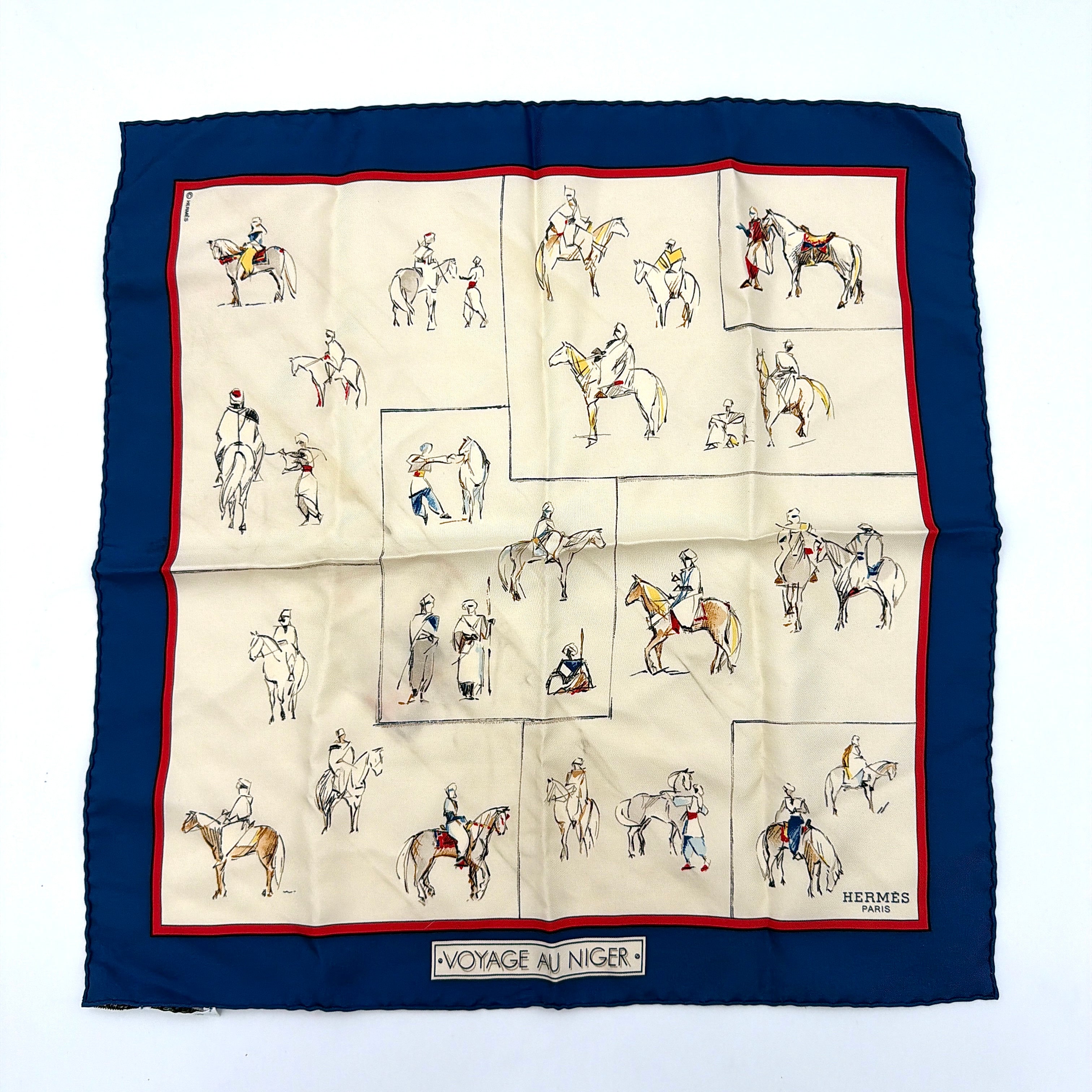Hermès Voyage au Niger silk scarf in navy blue with cream center, featuring illustrative equestrian sketches bordered in red.