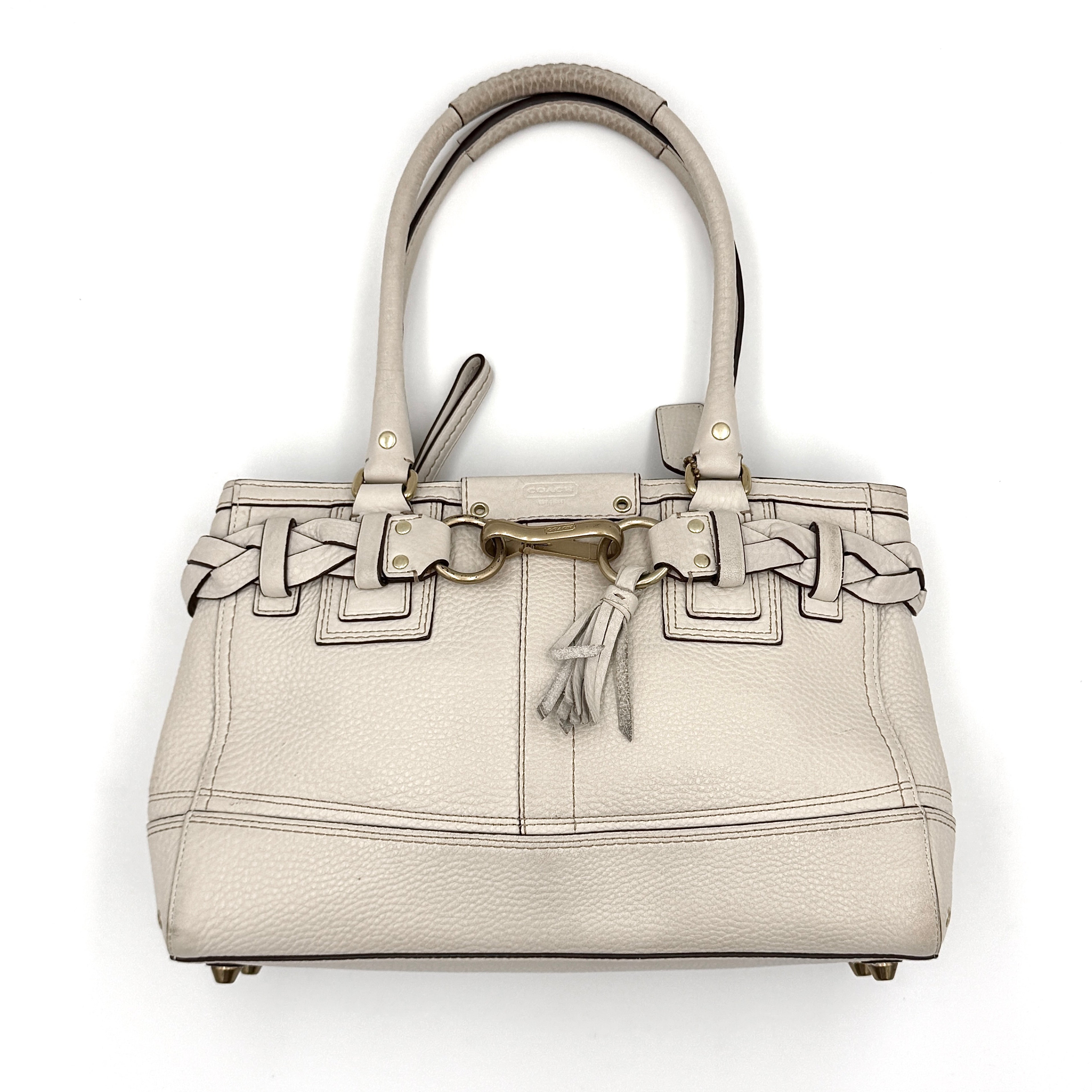 Coach Hampton Carryall in ivory leather with braided trim, brass dogleash clip, tassel, and top handles displayed against a white background.