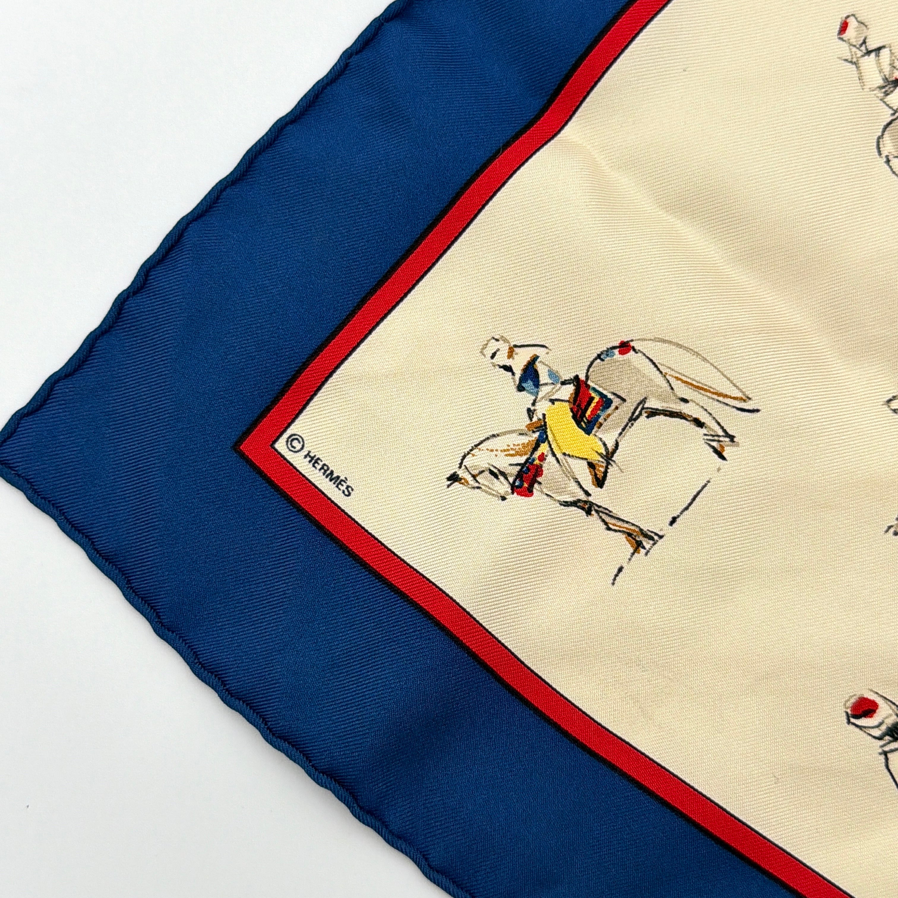 Hermès Voyage au Niger silk scarf in navy blue with cream center, featuring illustrative equestrian sketches bordered in red.
