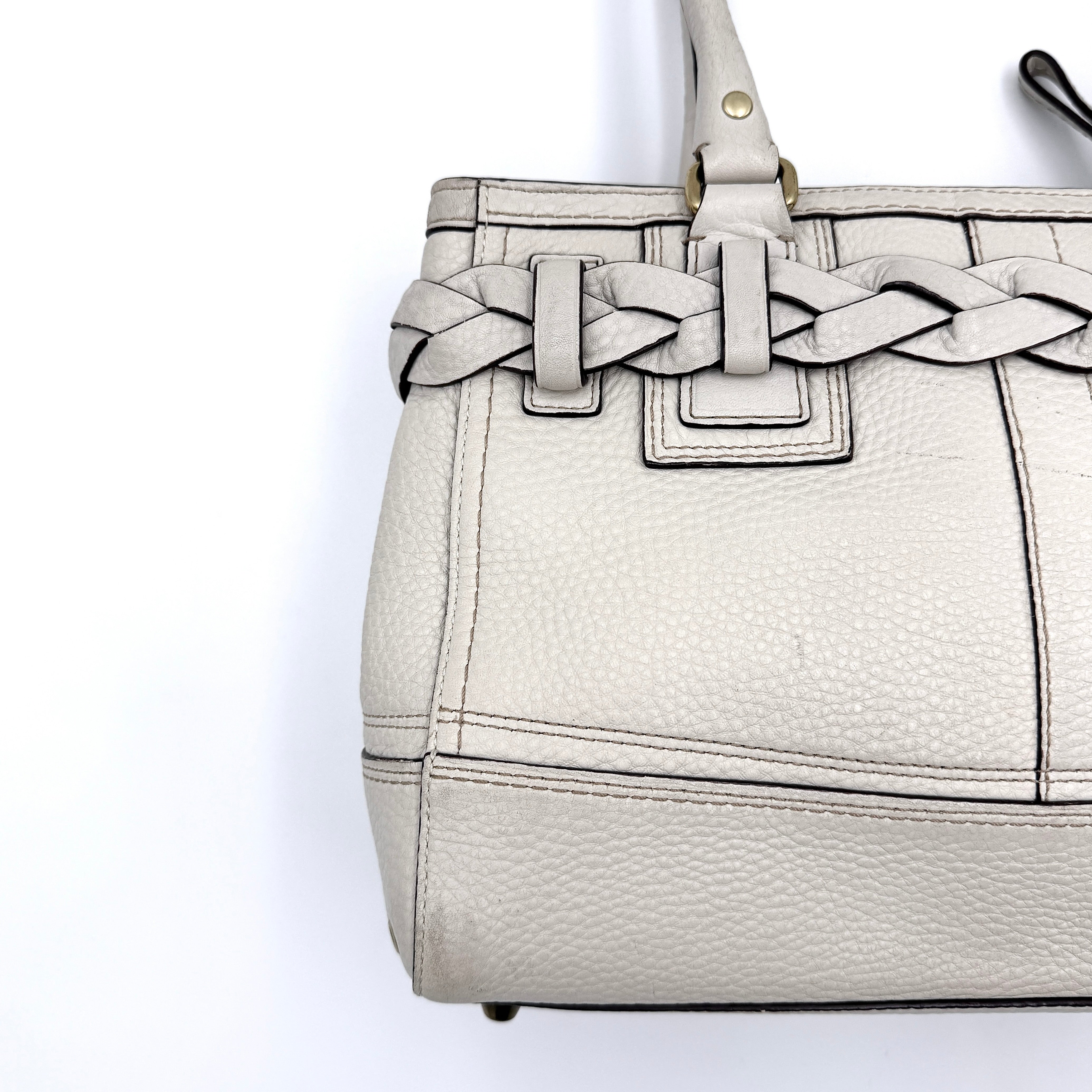 Coach Hampton Carryall in ivory leather with braided trim, brass dogleash clip, tassel, and top handles displayed against a white background.