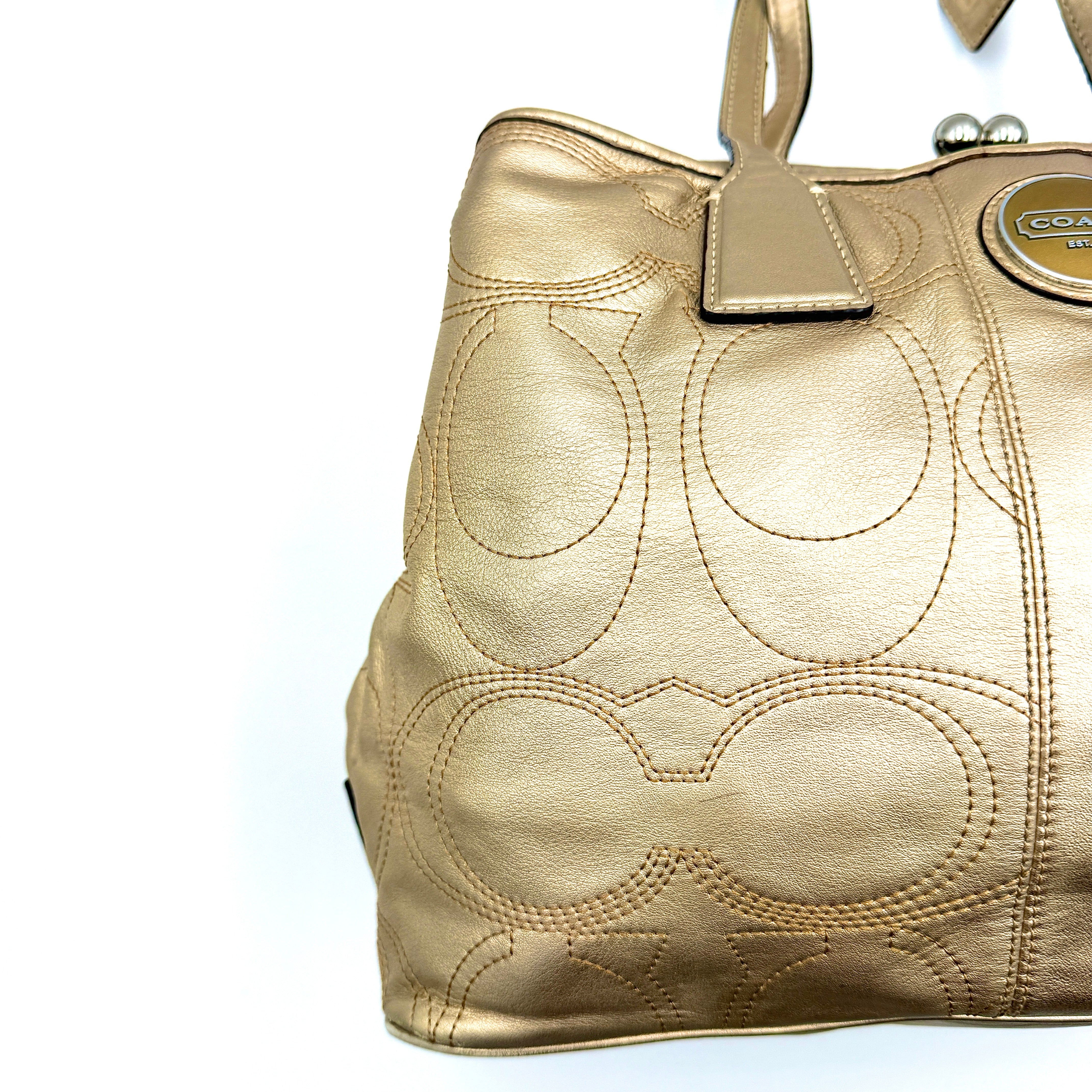 Coach metallic gold shoulder bag with signature embossed leather, double top handles, and a kisslock closure set against a clean background.
