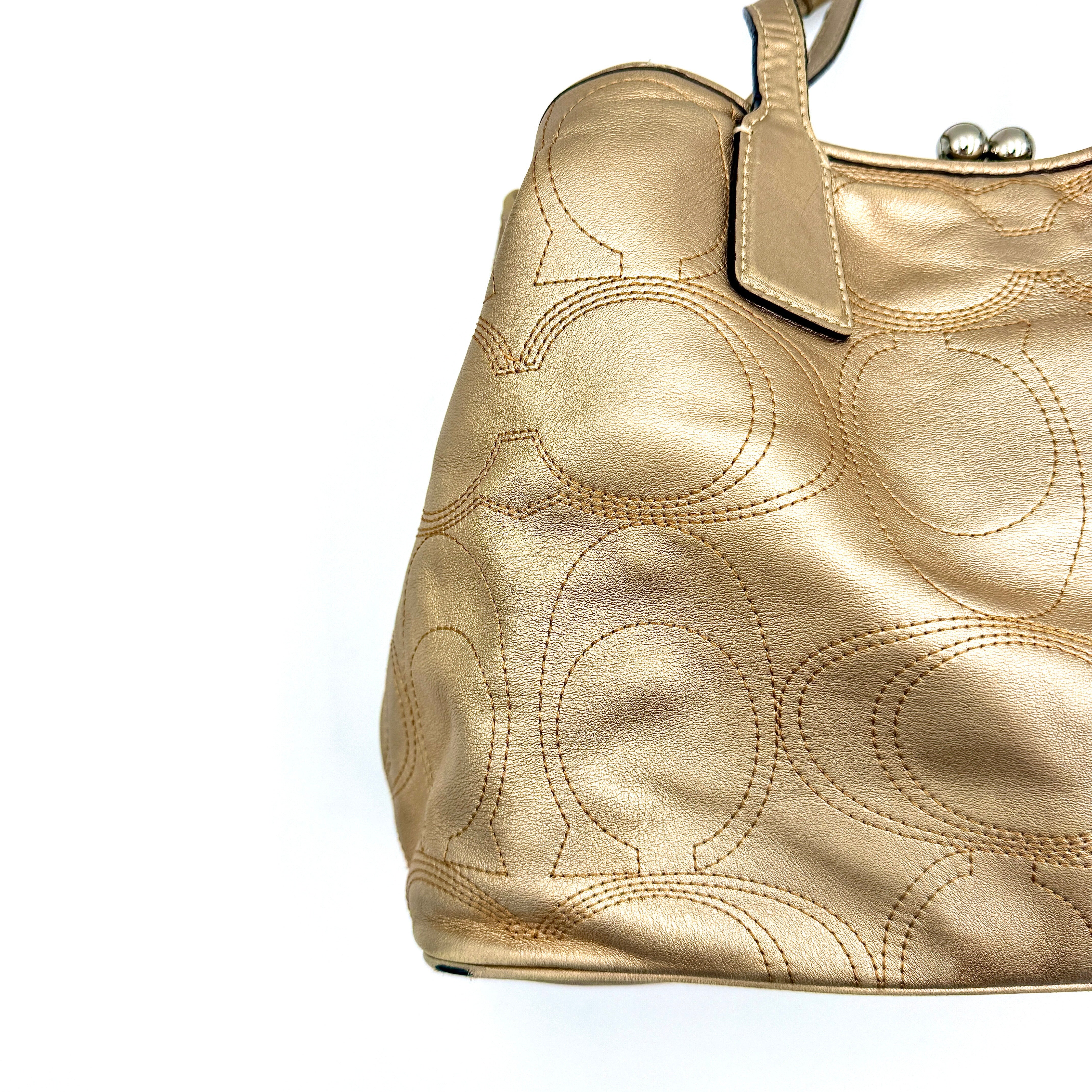 Coach metallic gold shoulder bag with signature embossed leather, double top handles, and a kisslock closure set against a clean background.