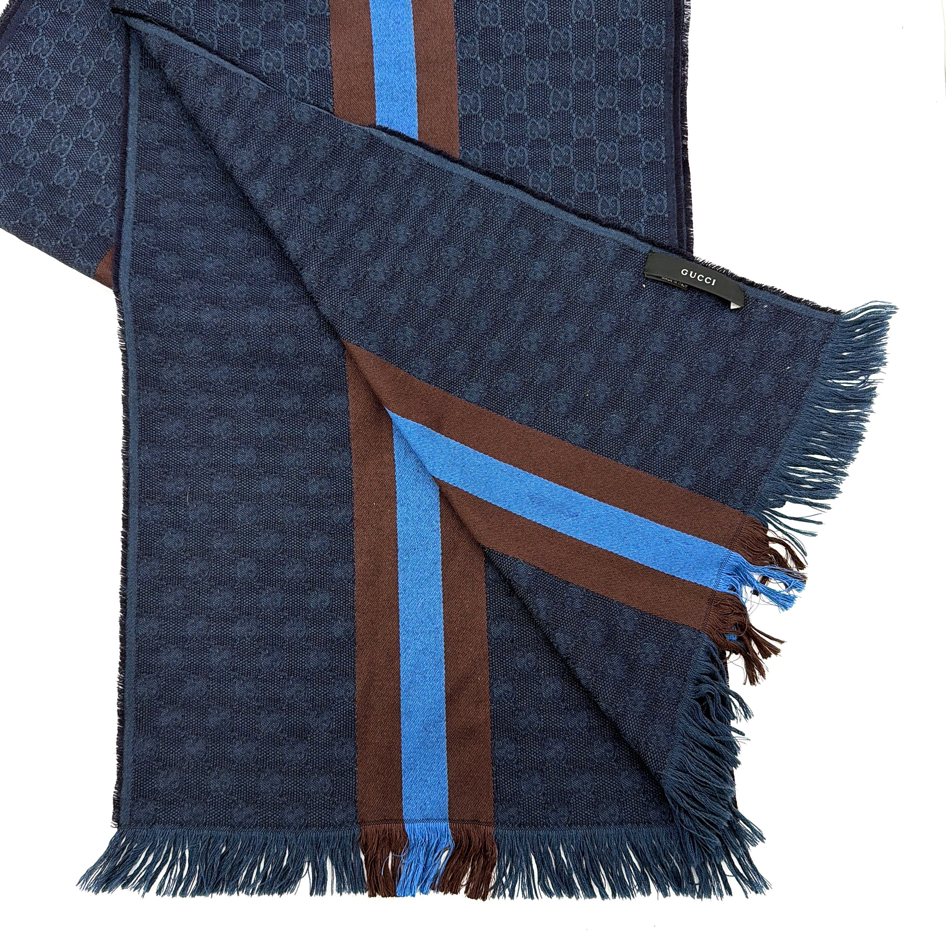 Gucci GG Monogram navy blue scarf with brown and blue Sherry Web stripes and fringed edges, artfully arranged to showcase its luxurious texture.