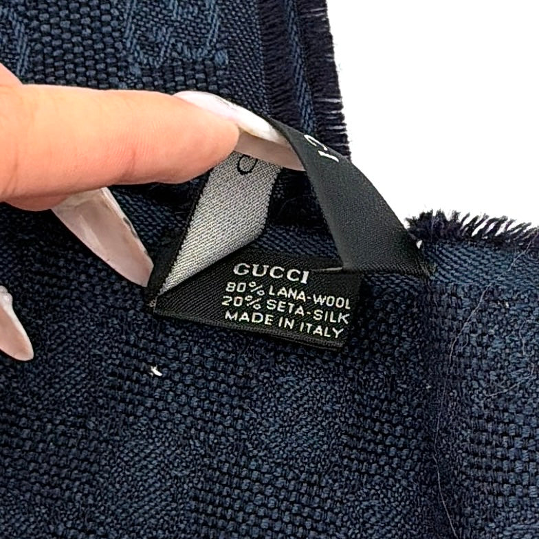 Gucci GG Monogram navy blue scarf with brown and blue Sherry Web stripes and fringed edges, artfully arranged to showcase its luxurious texture.