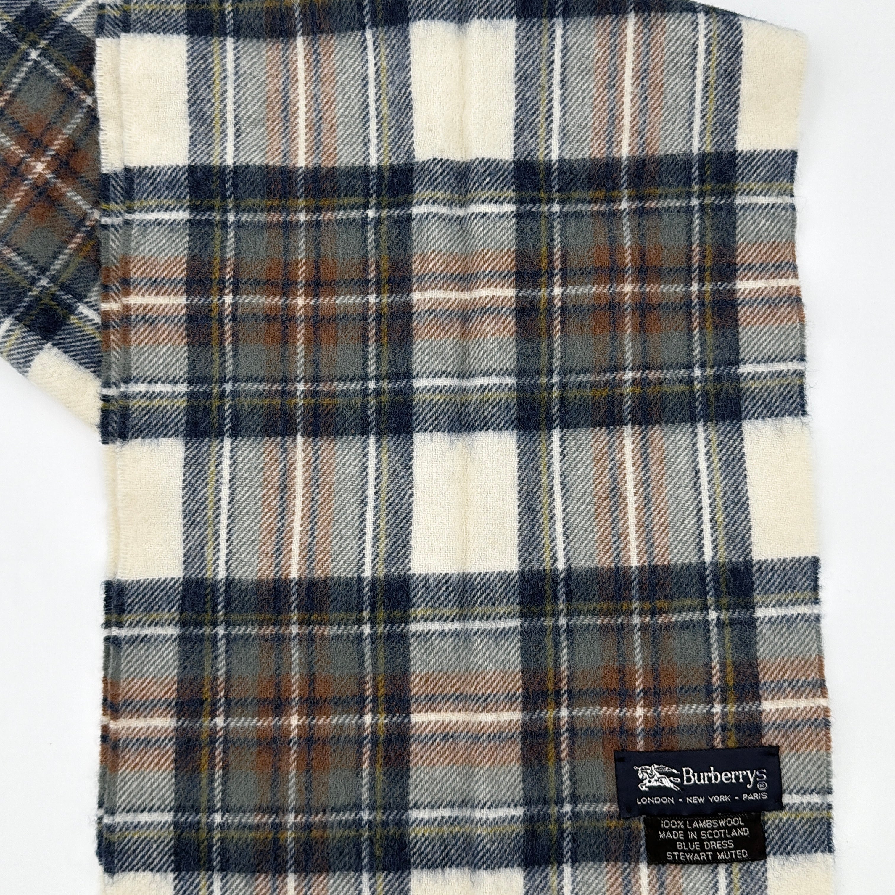 Burberry wool scarf in a muted blue, cream, and grey Stewart tartan, finished with long fringe and a woven heritage label.