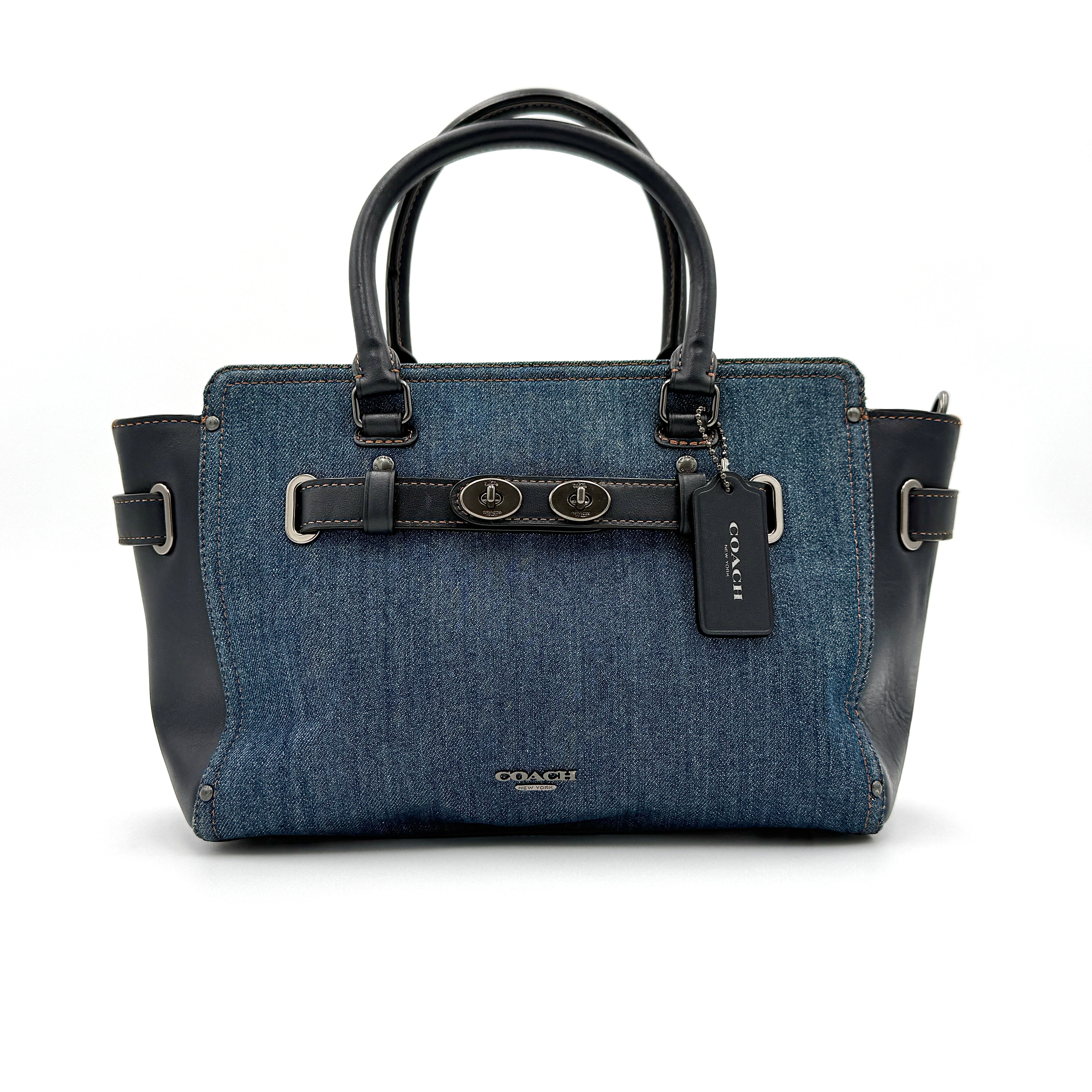 Coach Swagger 27 handbag in blue denim with navy leather trim and detachable strap, featuring prominent double turn-lock hardware and floral interior.