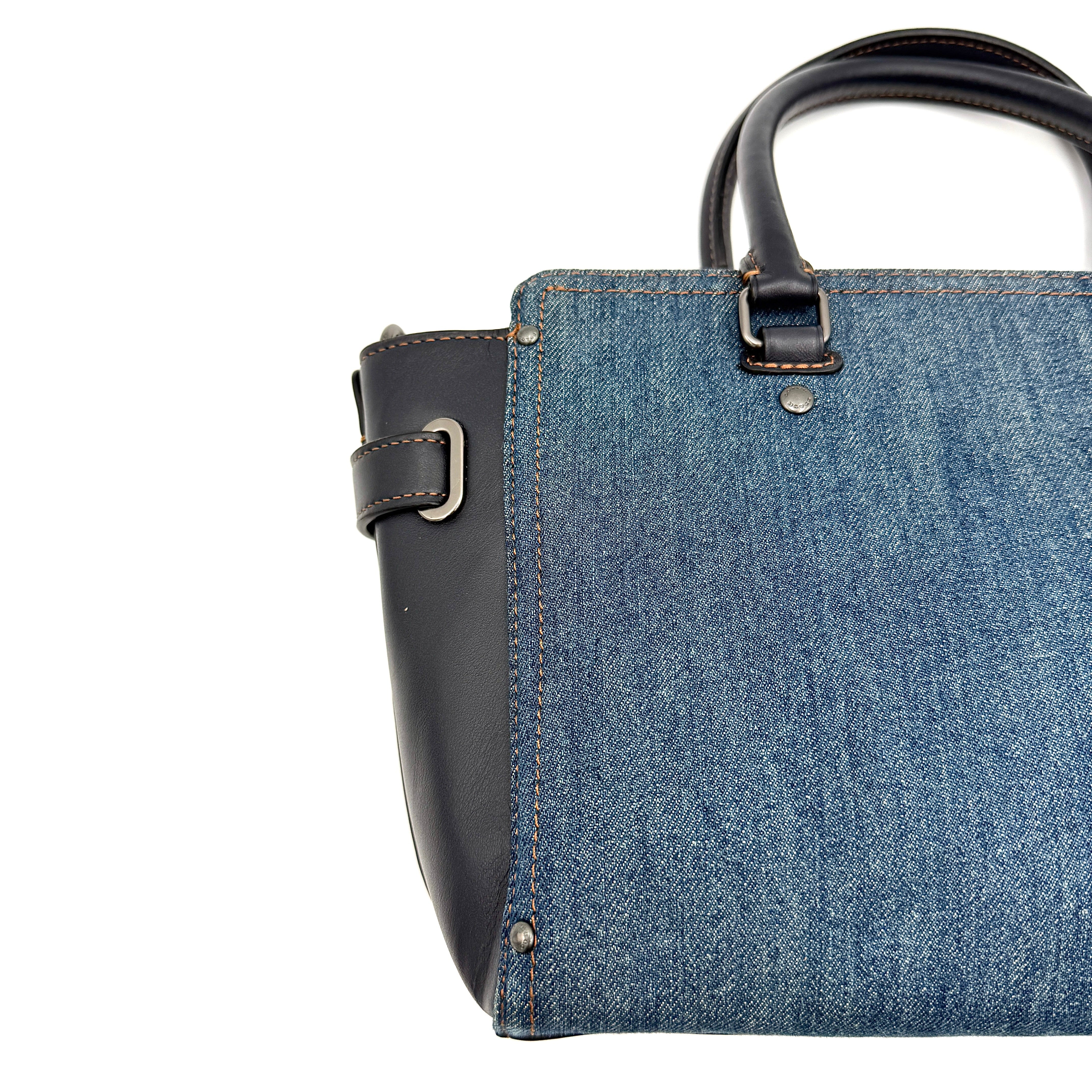 Coach Swagger 27 handbag in blue denim with navy leather trim and detachable strap, featuring prominent double turn-lock hardware and floral interior.