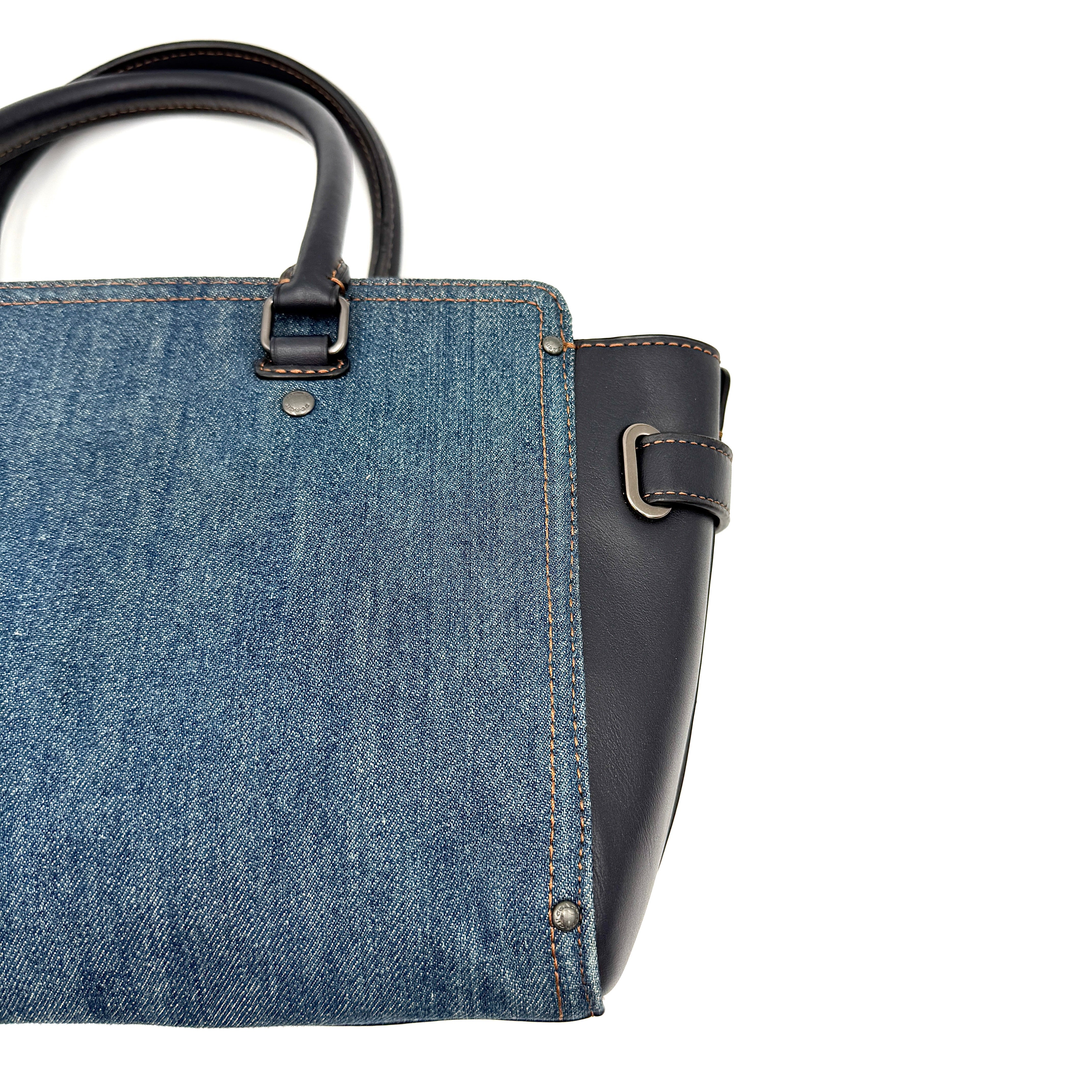 Coach Swagger 27 handbag in blue denim with navy leather trim and detachable strap, featuring prominent double turn-lock hardware and floral interior.