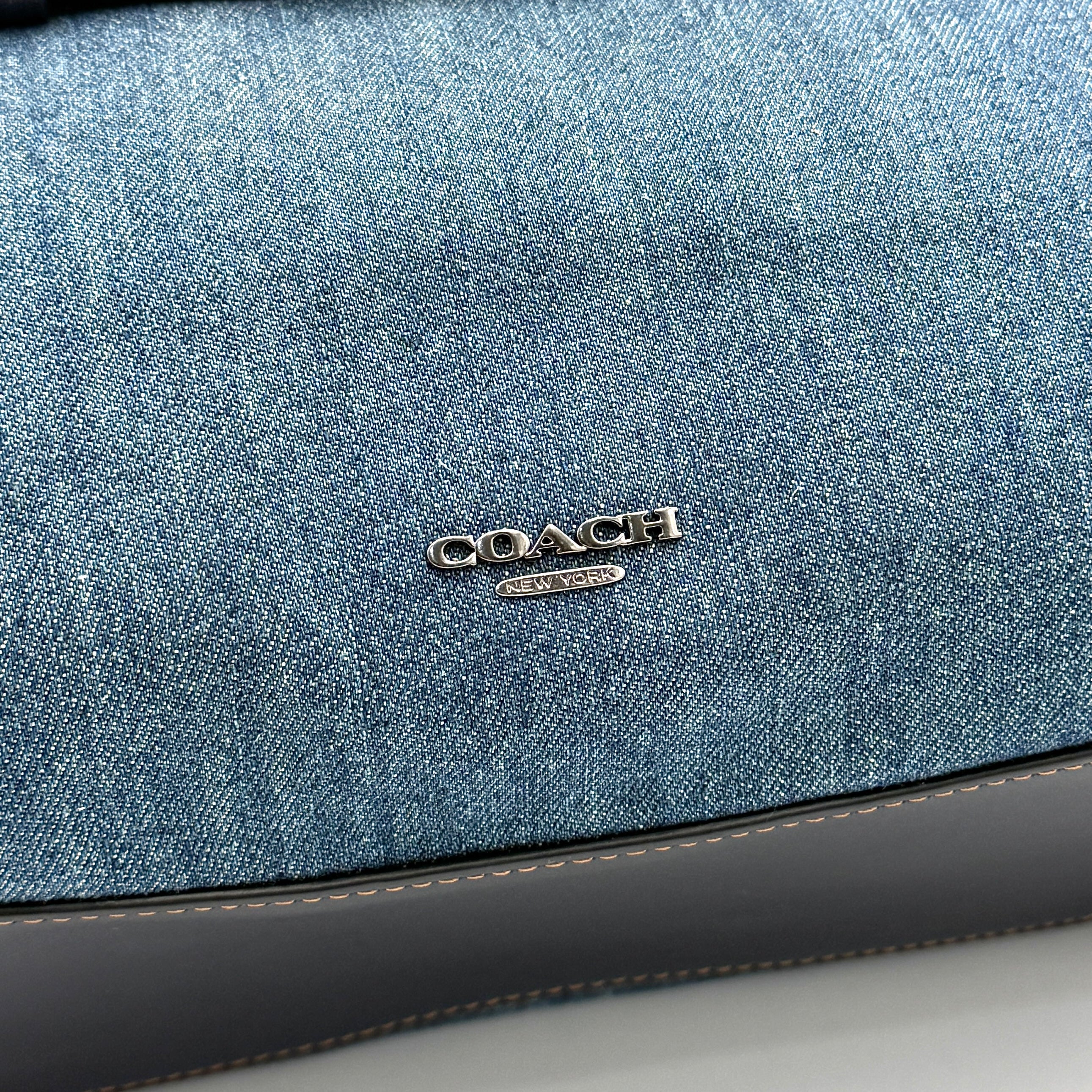 Coach Swagger 27 handbag in blue denim with navy leather trim and detachable strap, featuring prominent double turn-lock hardware and floral interior.