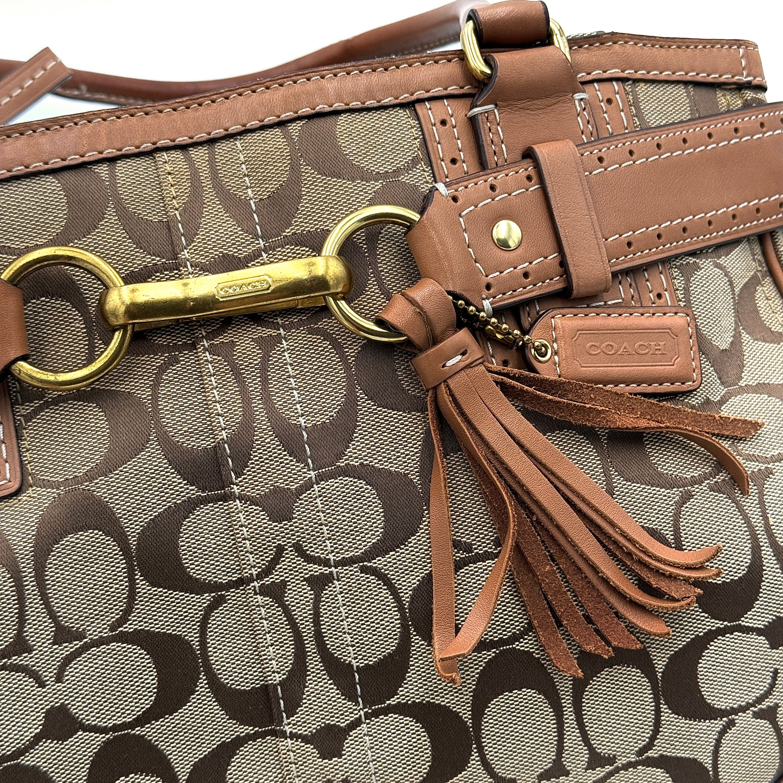 Coach Signature Hampton Carryall Shoulder Bag in beige and tan canvas with caramel leather trim, gold hardware, and tassel detail, shown standing upright.
