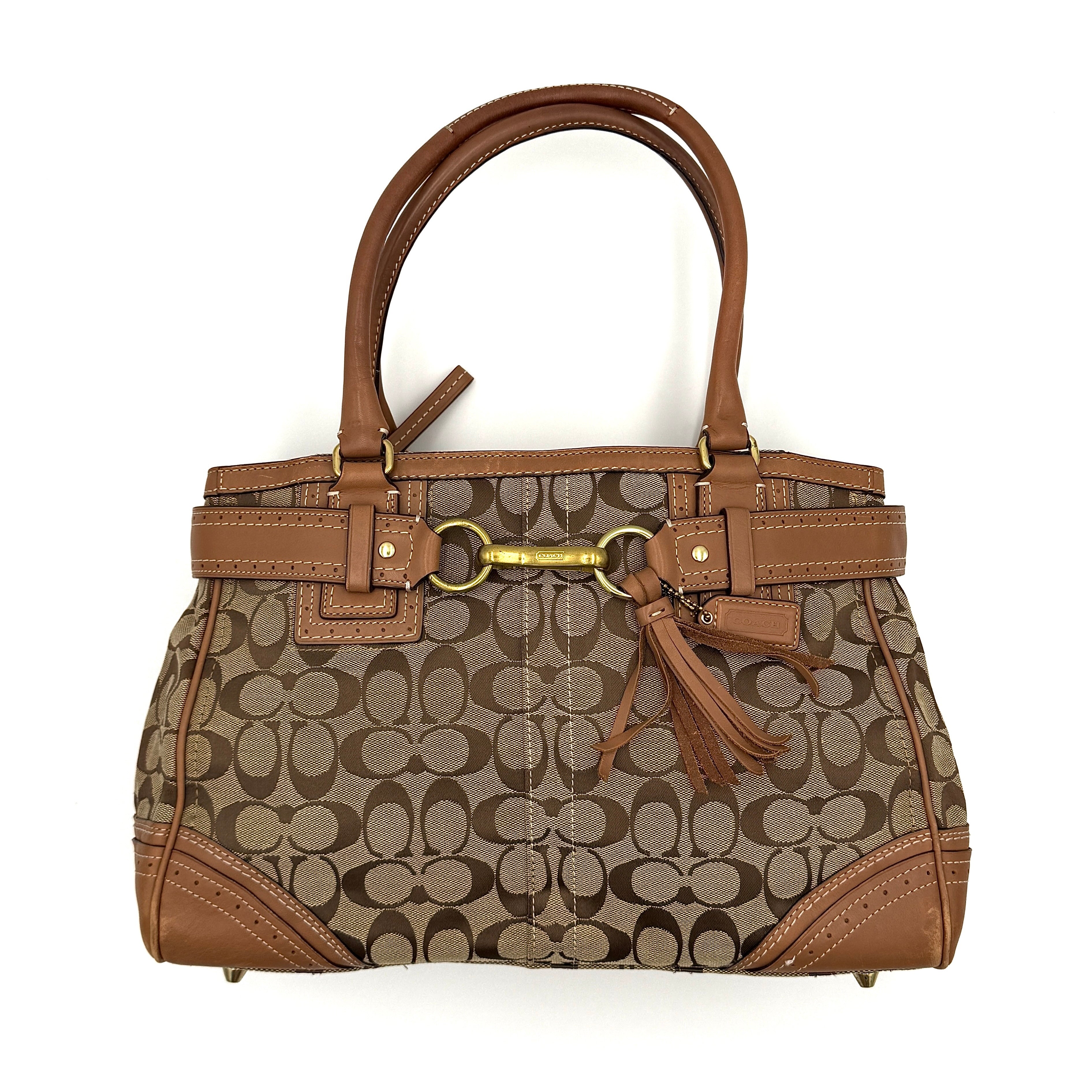 Coach Signature Hampton Carryall Shoulder Bag in beige and tan canvas with caramel leather trim, gold hardware, and tassel detail, shown standing upright.