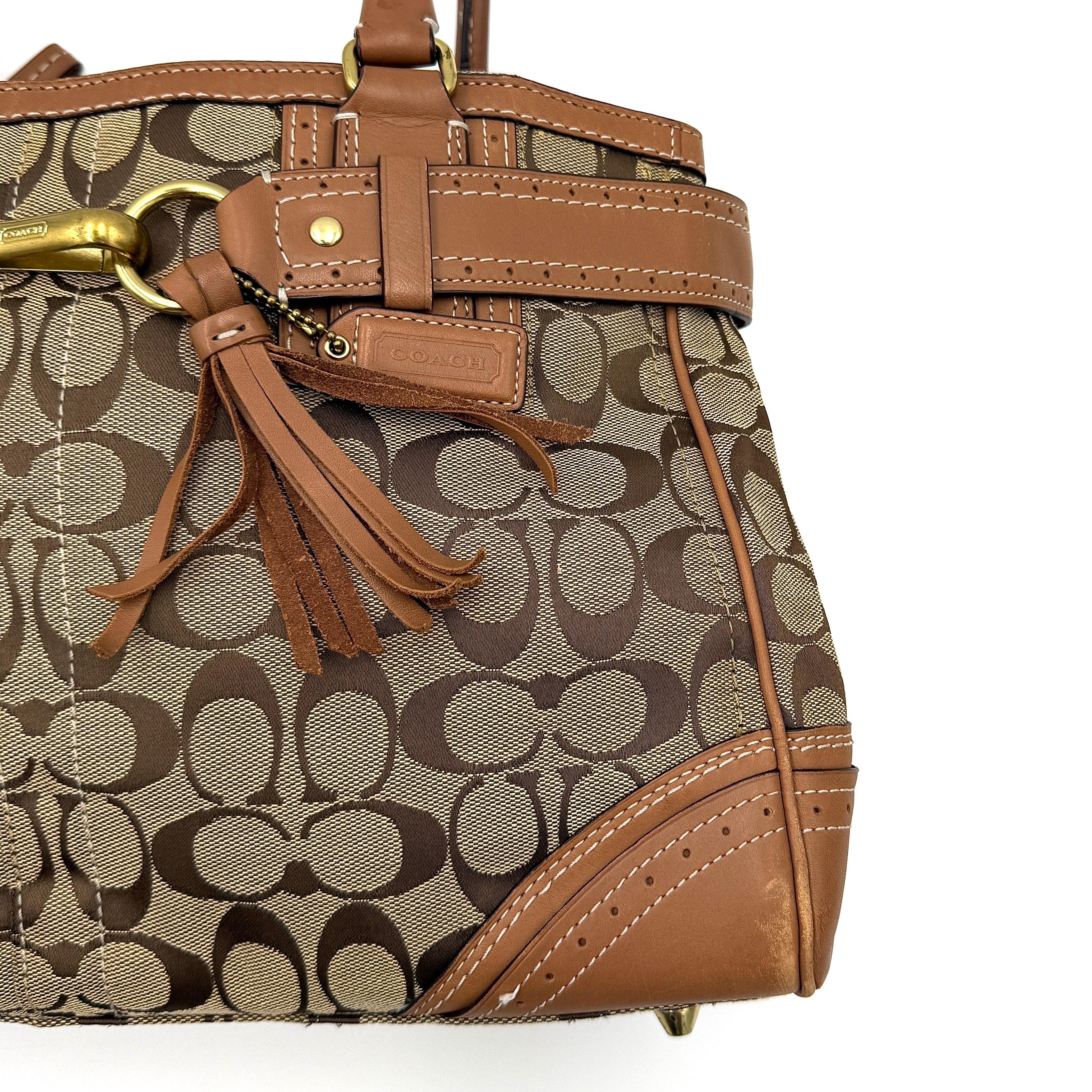 Coach Signature Hampton Carryall Shoulder Bag in beige and tan canvas with caramel leather trim, gold hardware, and tassel detail, shown standing upright.
