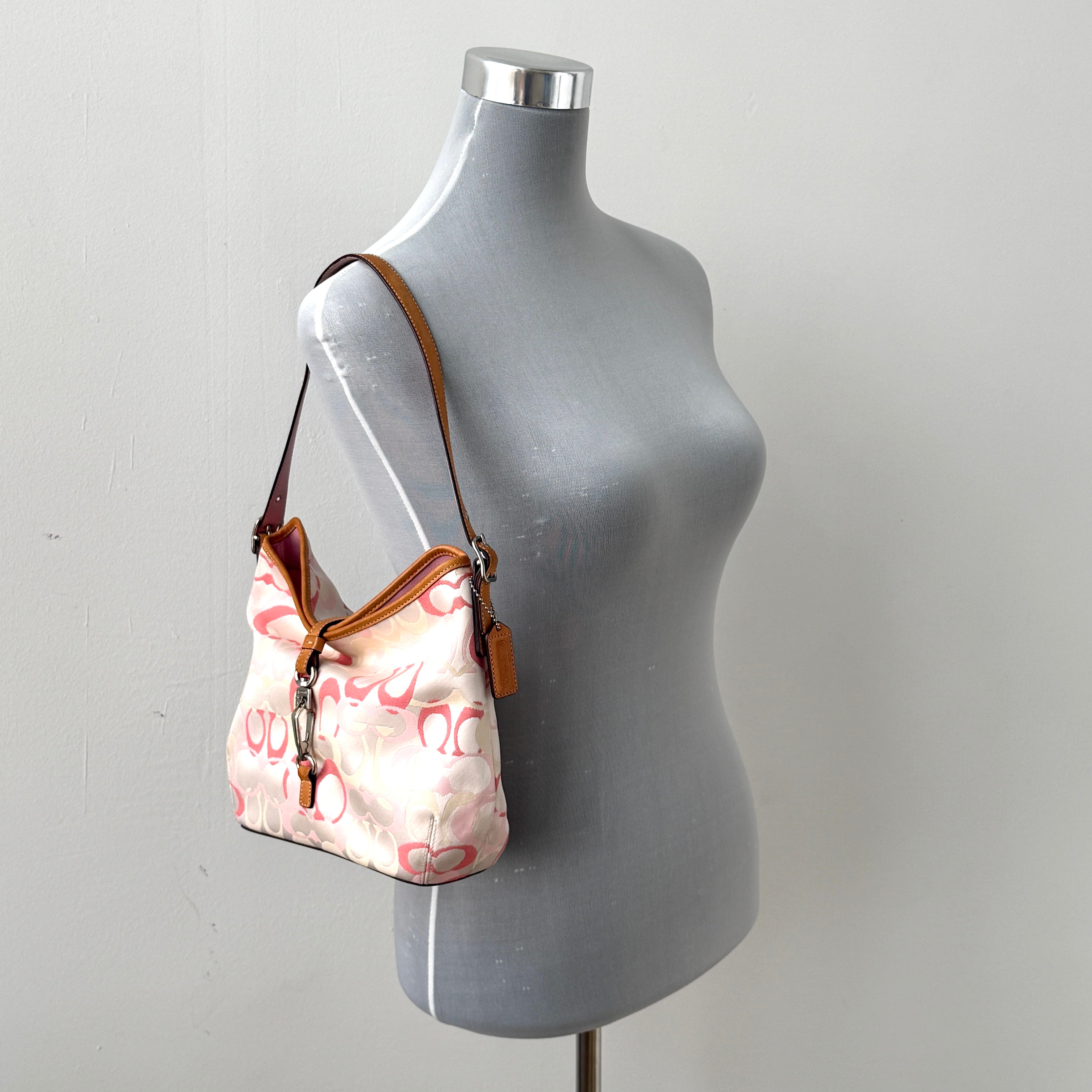 Coach hobo handbag in pink-cream canvas with signature C motif and tan leather trim, featuring a silver clip detail and a structured silhouette.