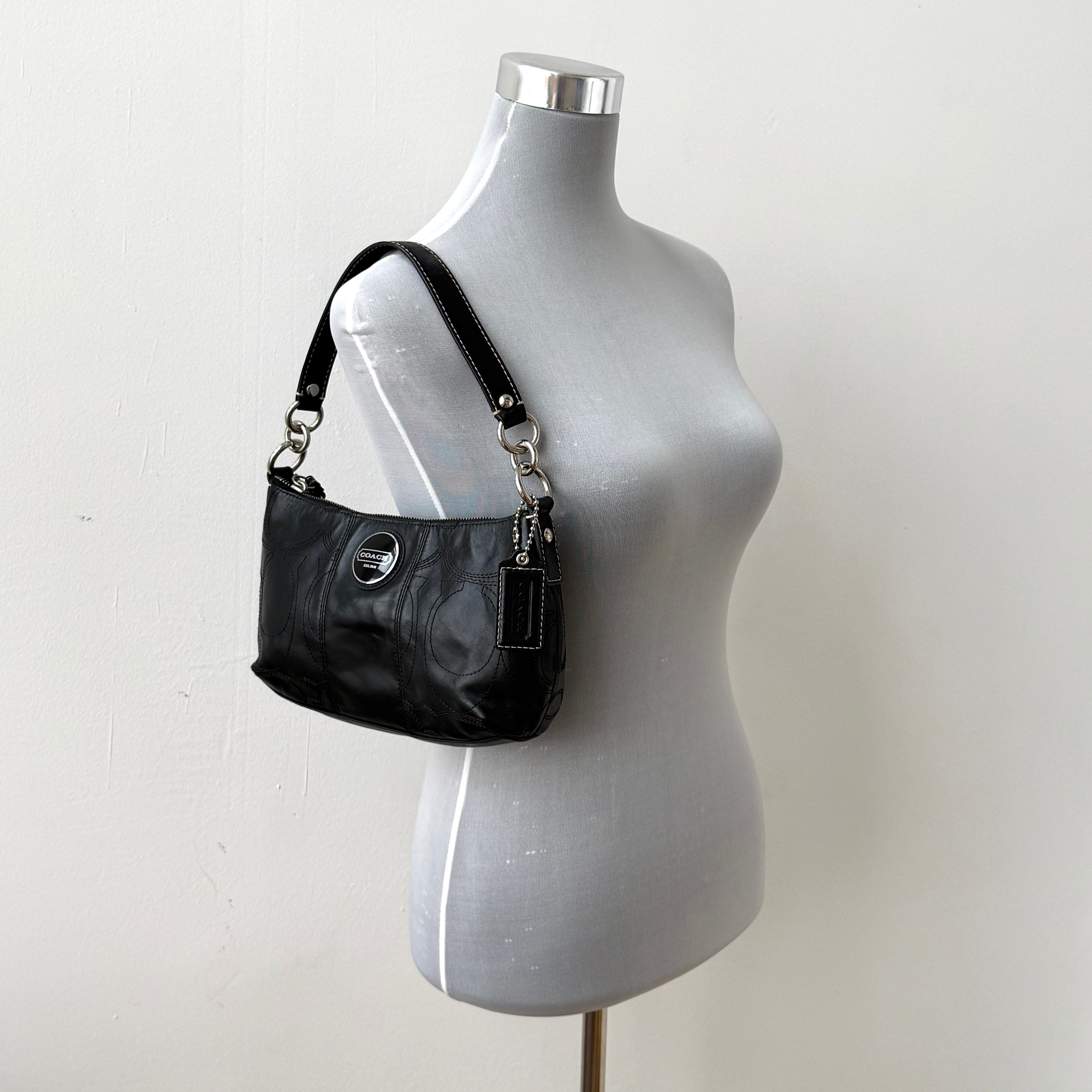 Coach black leather shoulder bag with signature embossed pattern and silver hardware, shown with attached logo tag and short leather strap.