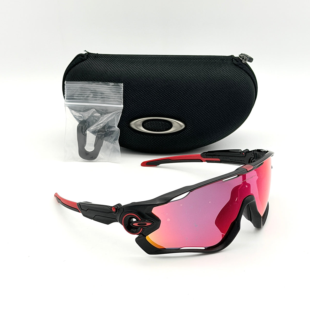 Oakley Jawbreaker Prizm sunglasses in matte black and red with pink-red Prizm lenses, shown with a black Oakley hard case and extra nose pad.