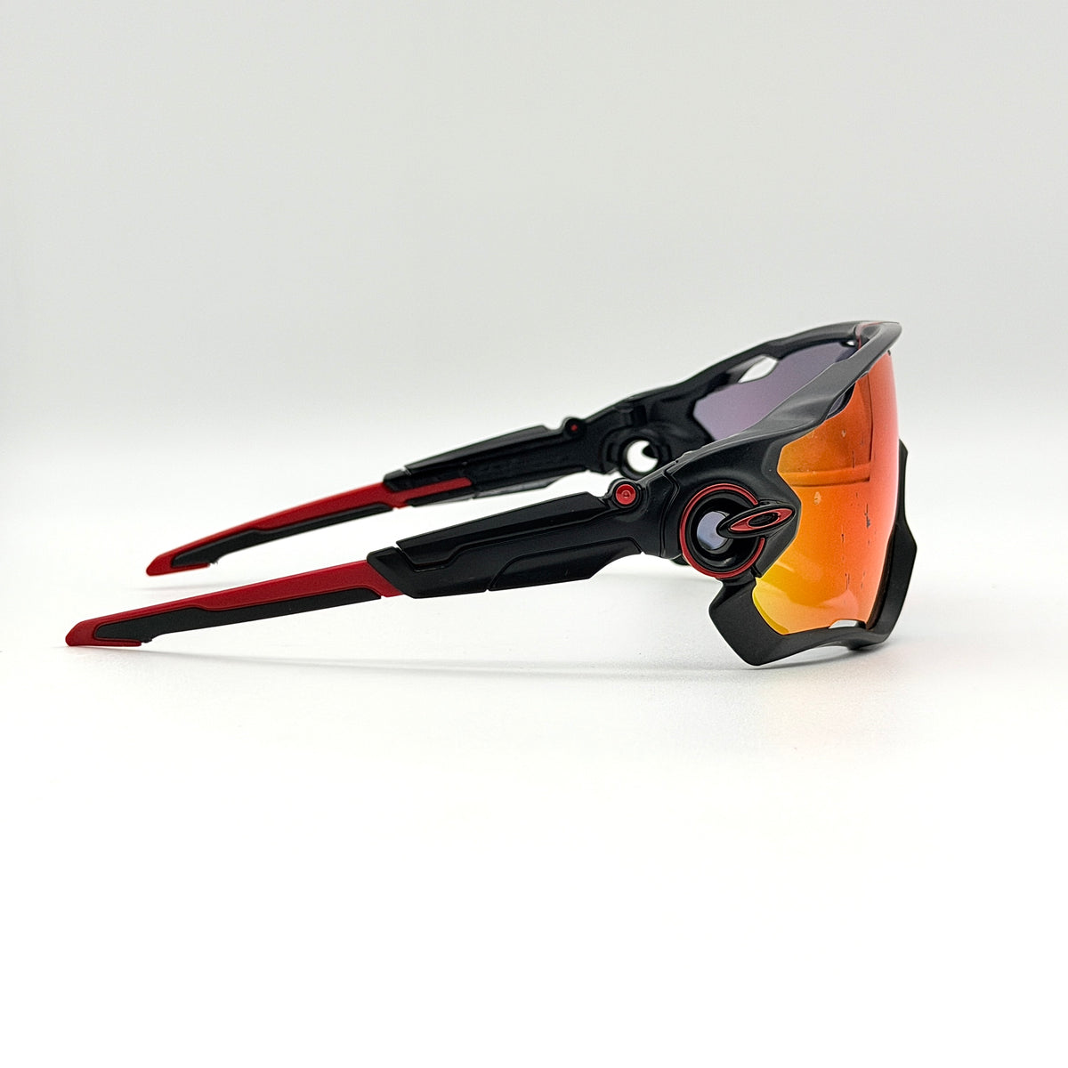 Oakley Jawbreaker Prizm sunglasses in matte black and red with pink-red Prizm lenses, shown with a black Oakley hard case and extra nose pad.