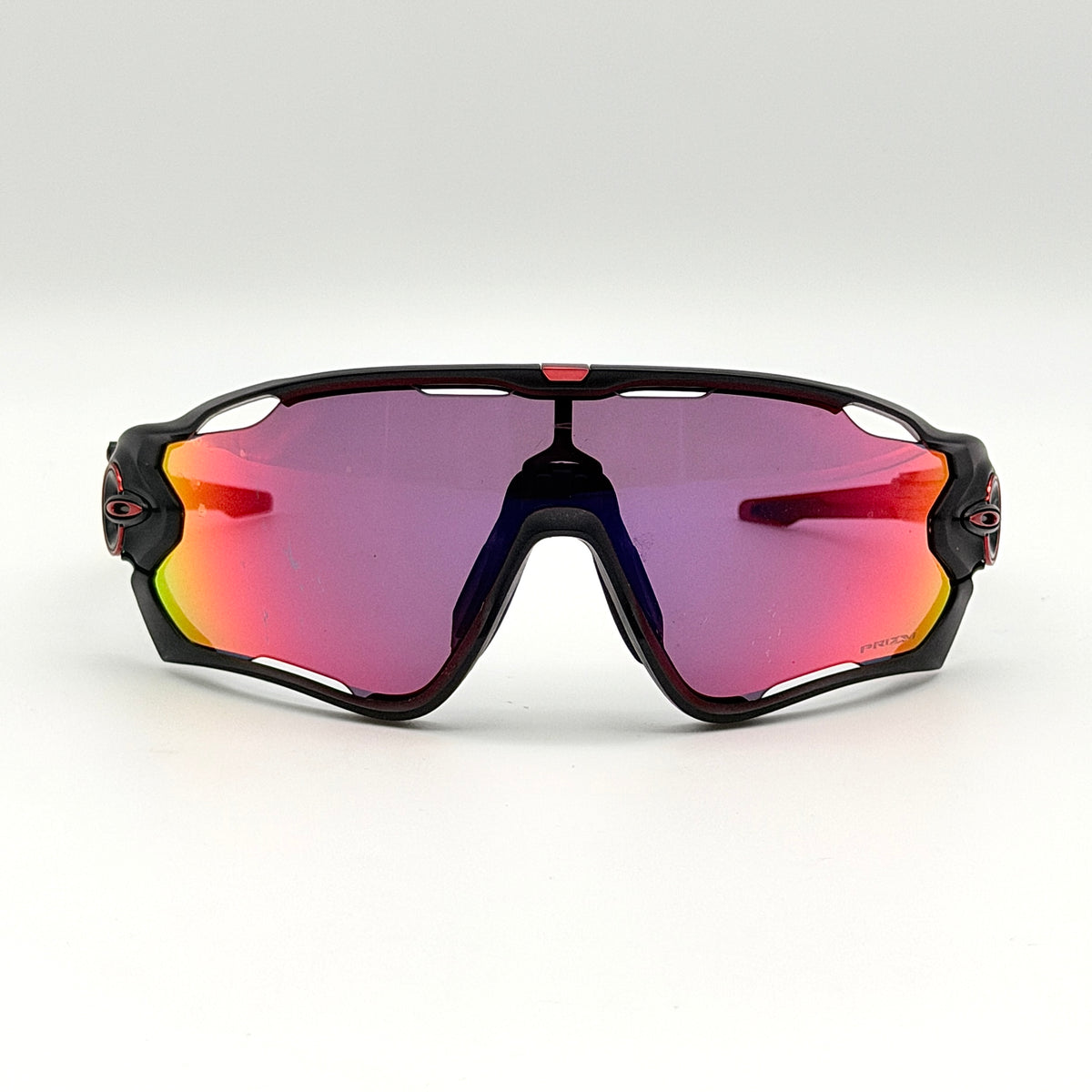 Oakley Jawbreaker Prizm sunglasses in matte black and red with pink-red Prizm lenses, shown with a black Oakley hard case and extra nose pad.