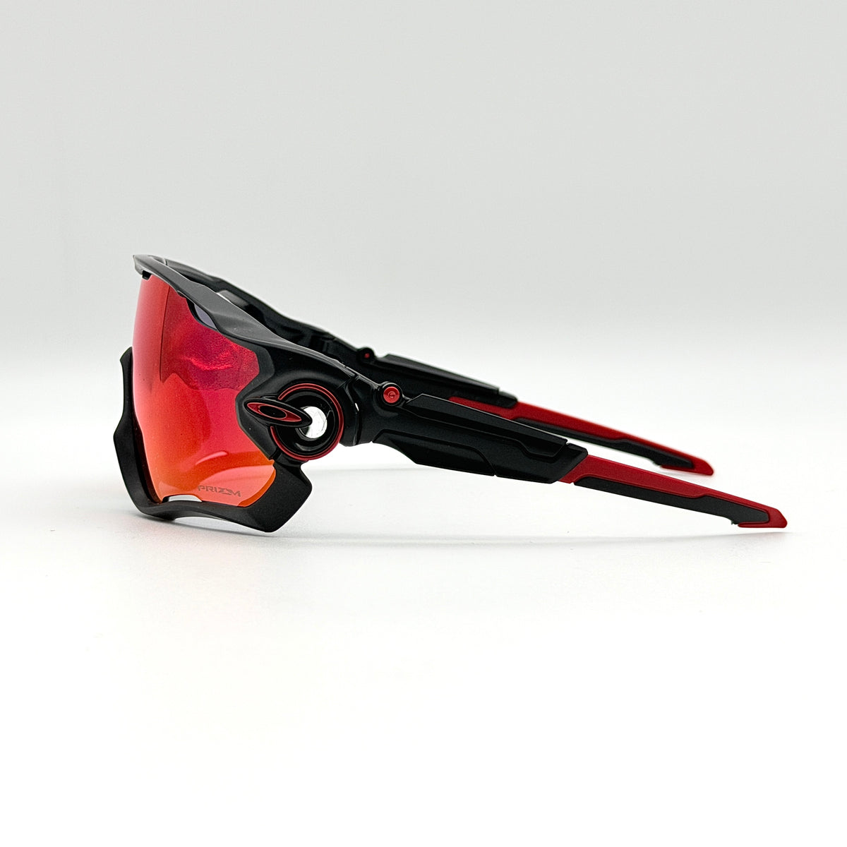 Oakley Jawbreaker Prizm sunglasses in matte black and red with pink-red Prizm lenses, shown with a black Oakley hard case and extra nose pad.