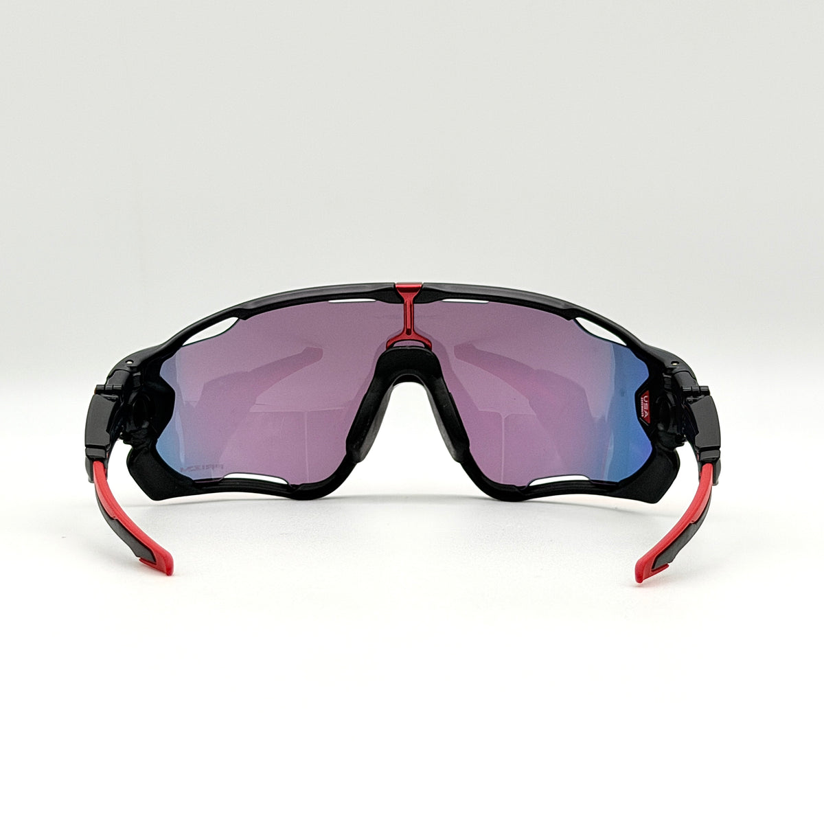 Oakley Jawbreaker Prizm sunglasses in matte black and red with pink-red Prizm lenses, shown with a black Oakley hard case and extra nose pad.