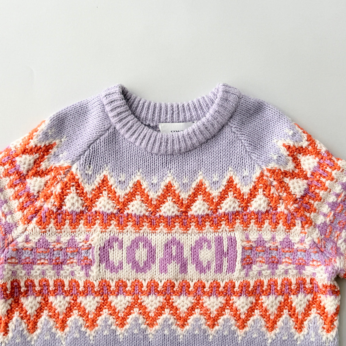 Coach Fair Isle Ski Sweater in lilac with orange and cream geometric pattern and COACH logo across the chest.