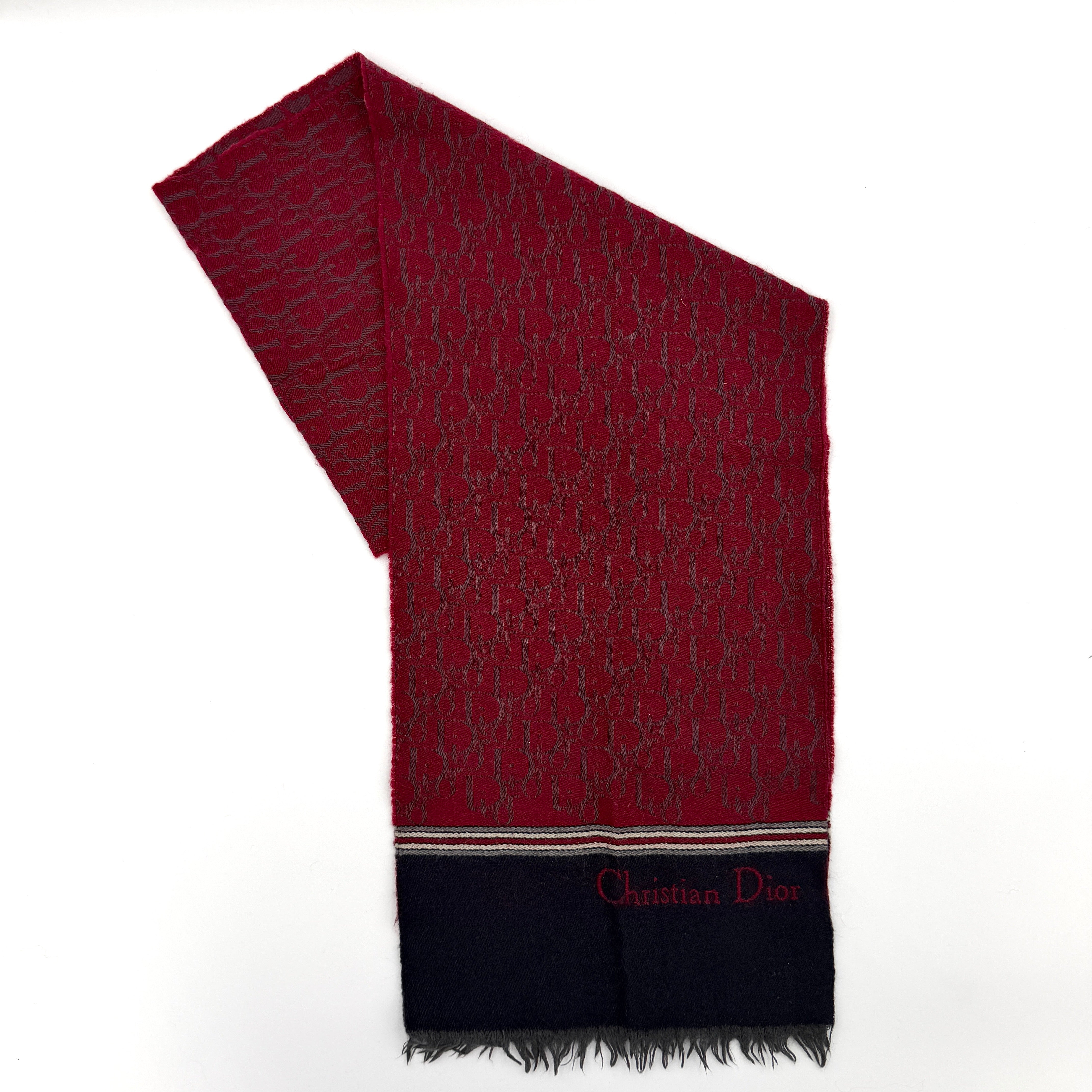 A red Dior Oblique Trotter wool scarf with all-over monogram pattern, navy border, stripe detail, and fringe trim.