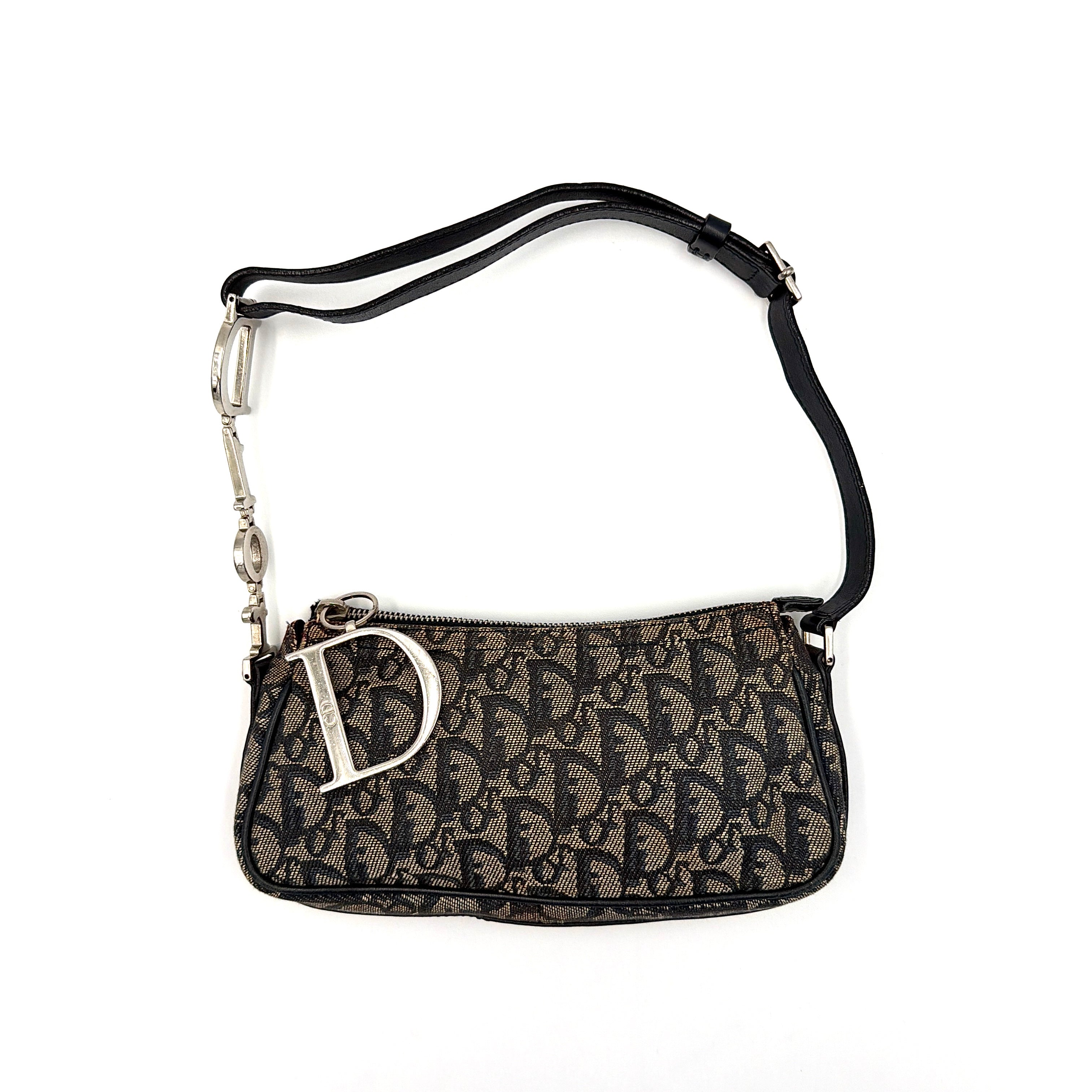 Dior Trotter Charm Pochette bag in grey and navy oblique canvas, featuring bold silver-tone Dior letter charms and a black leather strap.