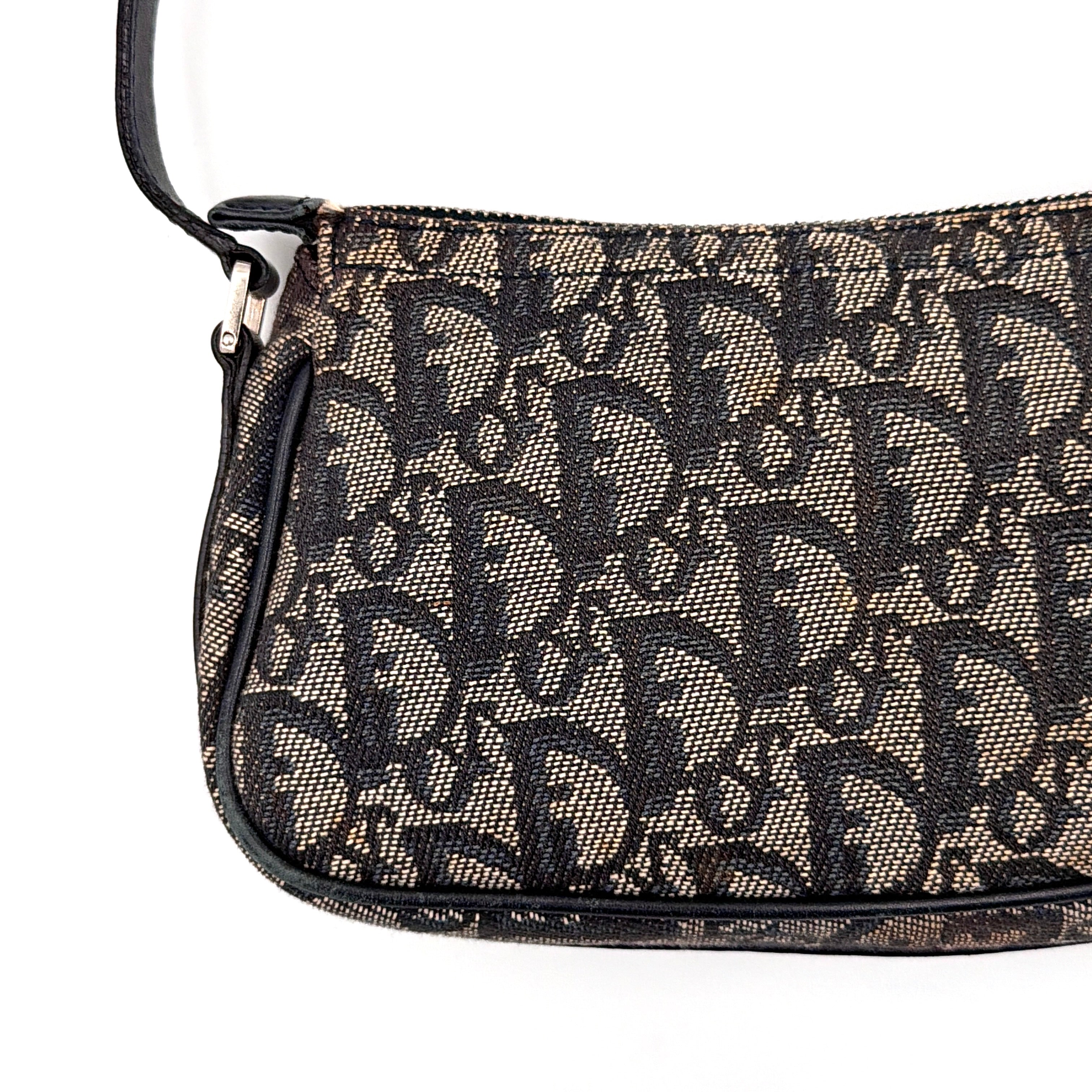 Dior Trotter Charm Pochette bag in grey and navy oblique canvas, featuring bold silver-tone Dior letter charms and a black leather strap.