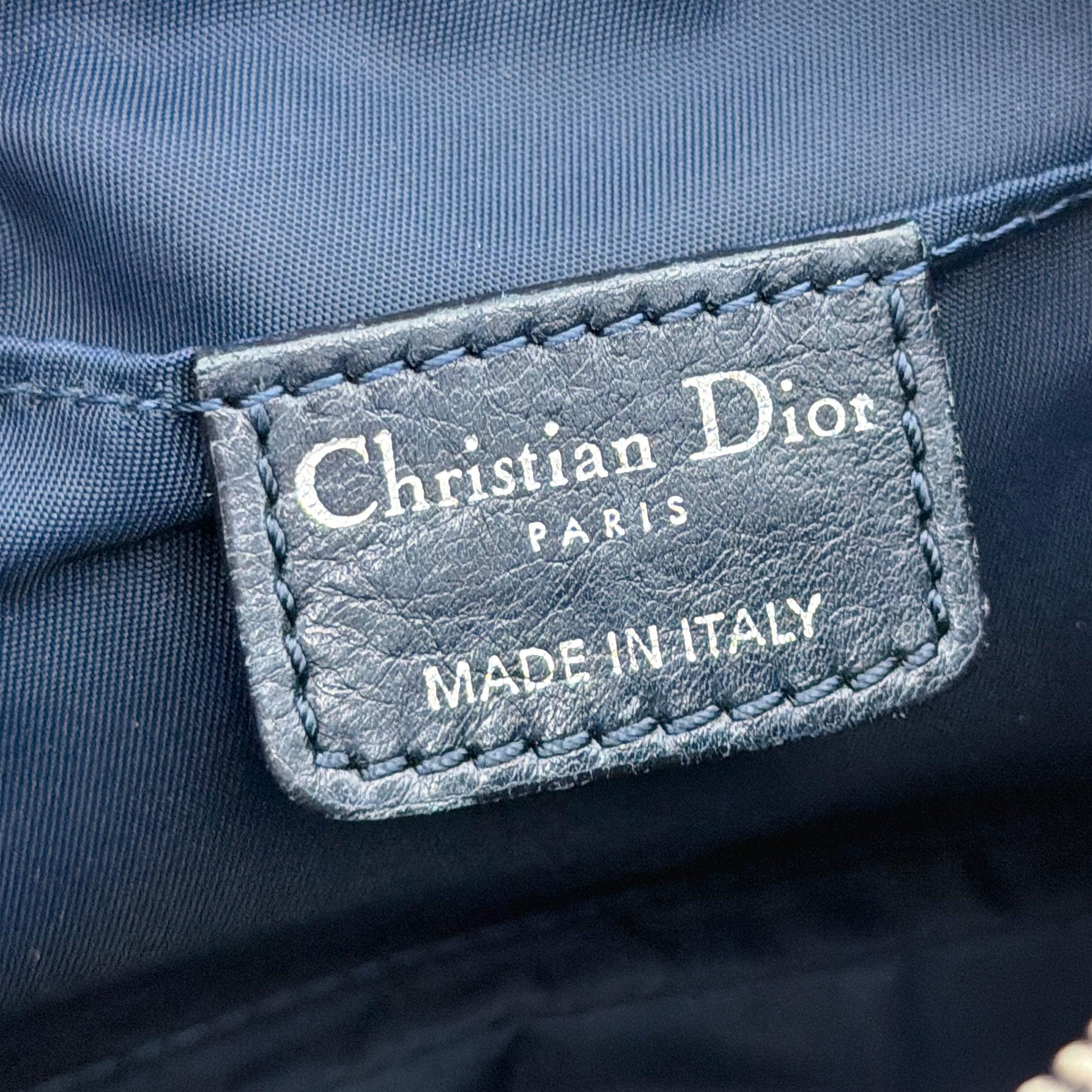 Dior Trotter Charm Pochette bag in grey and navy oblique canvas, featuring bold silver-tone Dior letter charms and a black leather strap.