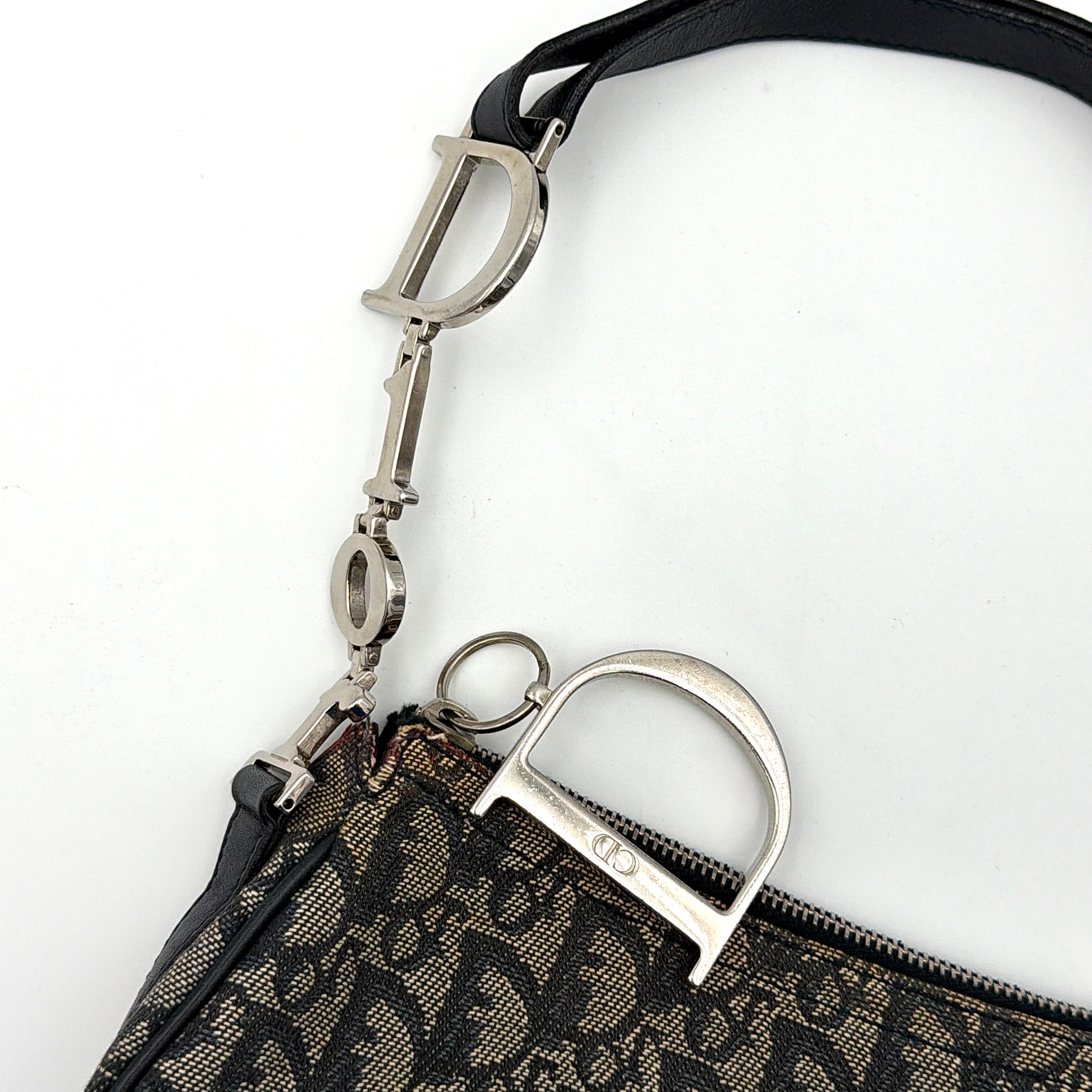 Dior Trotter Charm Pochette bag in grey and navy oblique canvas, featuring bold silver-tone Dior letter charms and a black leather strap.