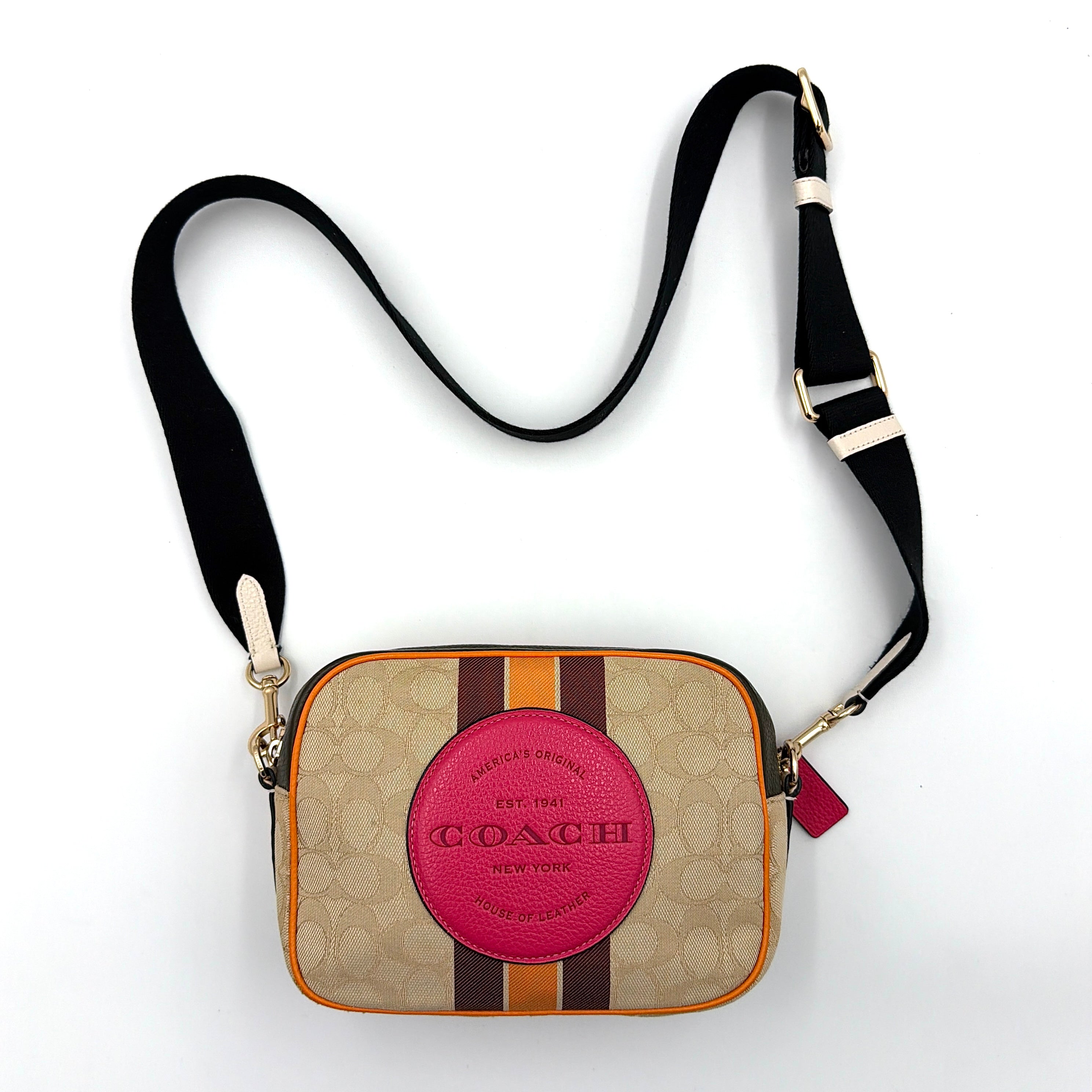 Coach Signature Dempsey Camera Bag in monogram canvas with bold pink logo patch, orange stripes, and wide black strap.