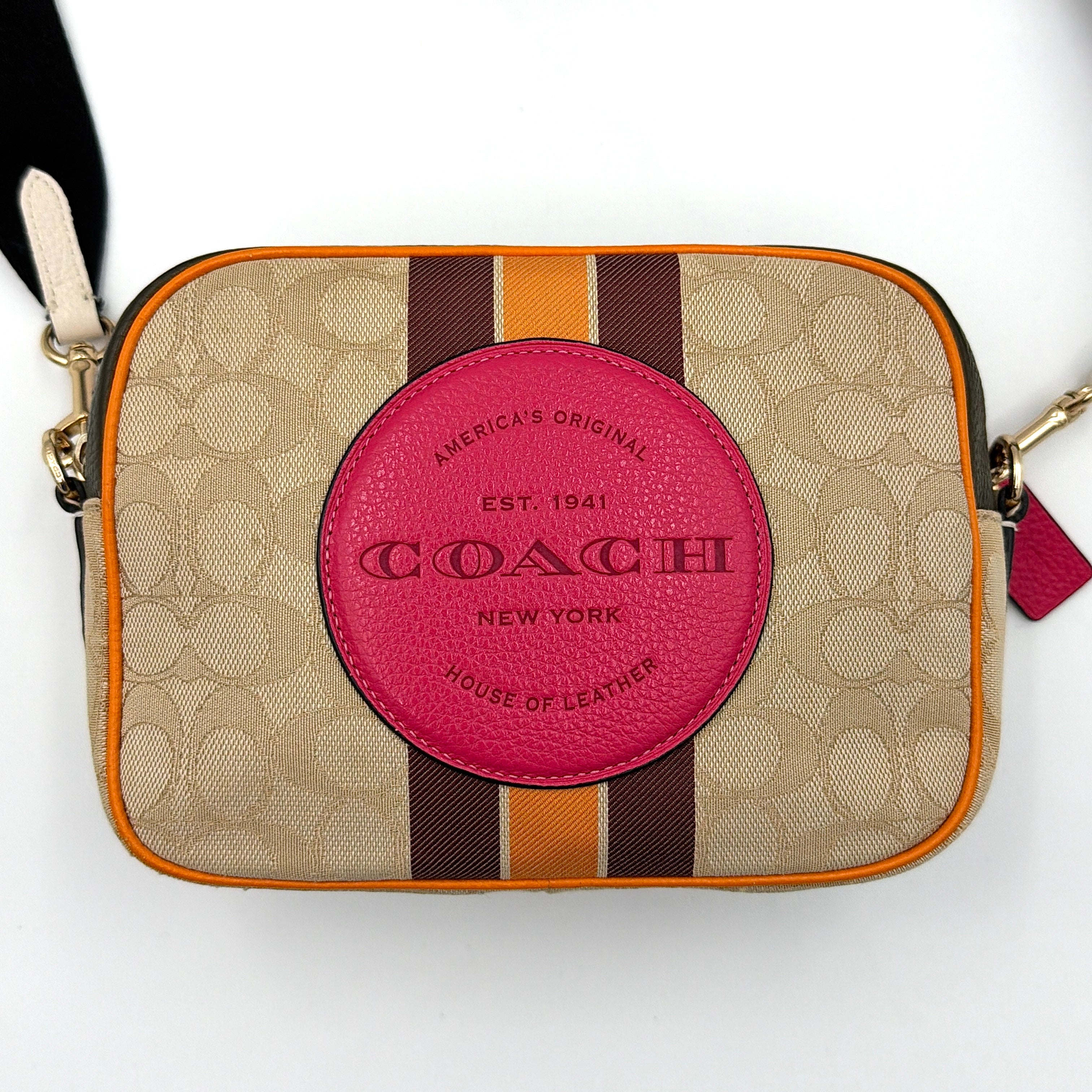 Coach Signature Dempsey Camera Bag in monogram canvas with bold pink logo patch, orange stripes, and wide black strap.