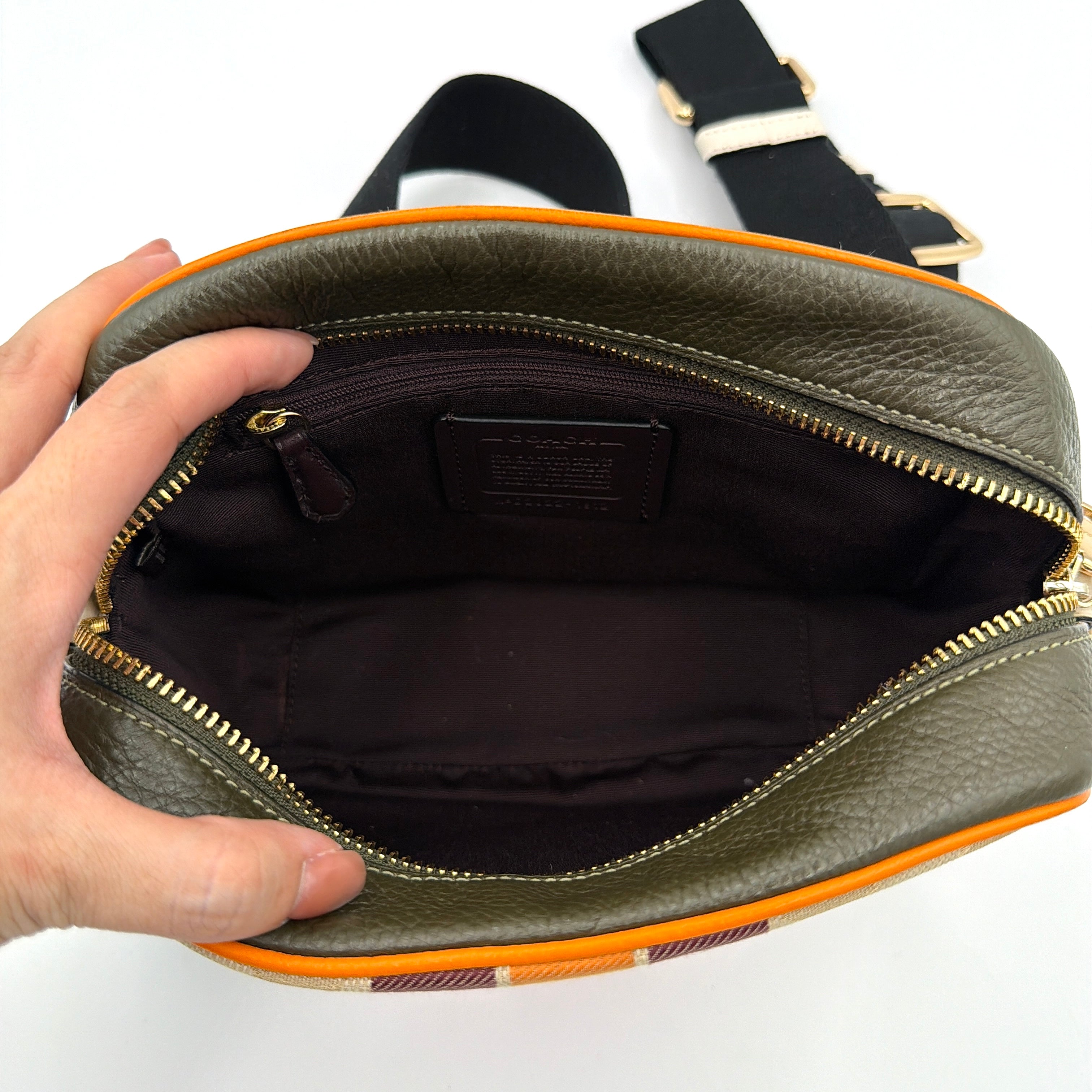 Coach Signature Dempsey Camera Bag in monogram canvas with bold pink logo patch, orange stripes, and wide black strap.