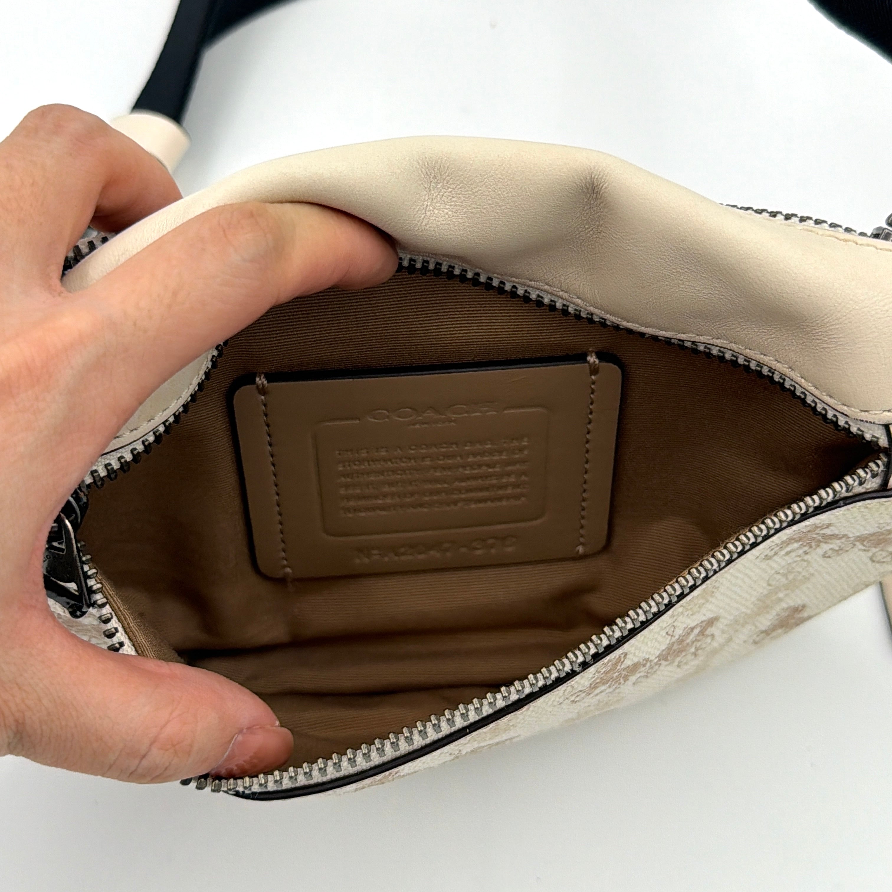 Coach Mini Warren belt bag in cream canvas with tan horse and carriage motif, leather trim, and black adjustable strap.
