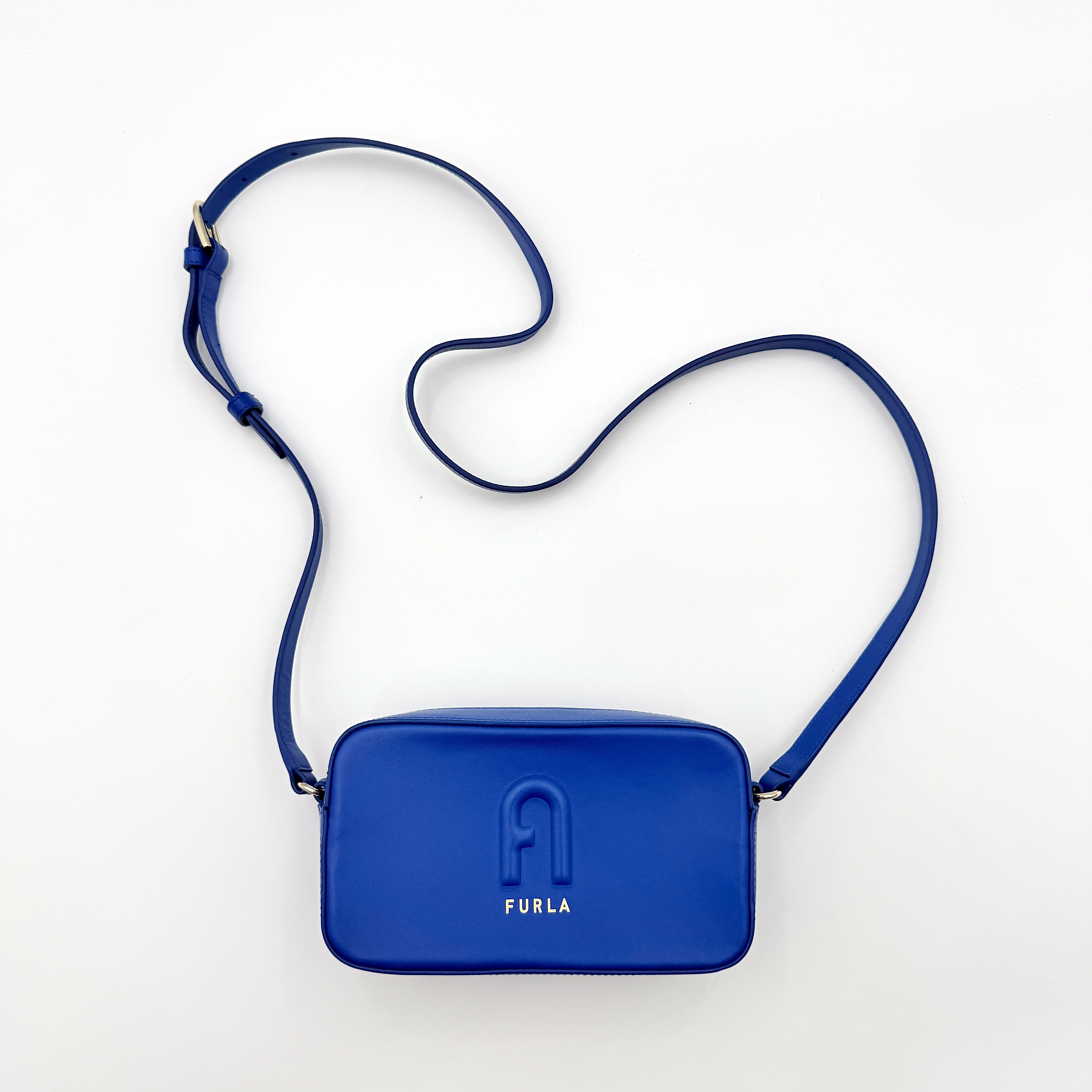 Furla Primula Mini Camera Crossbody Bag in vibrant blue leather with embossed logo, shown with adjustable strap.