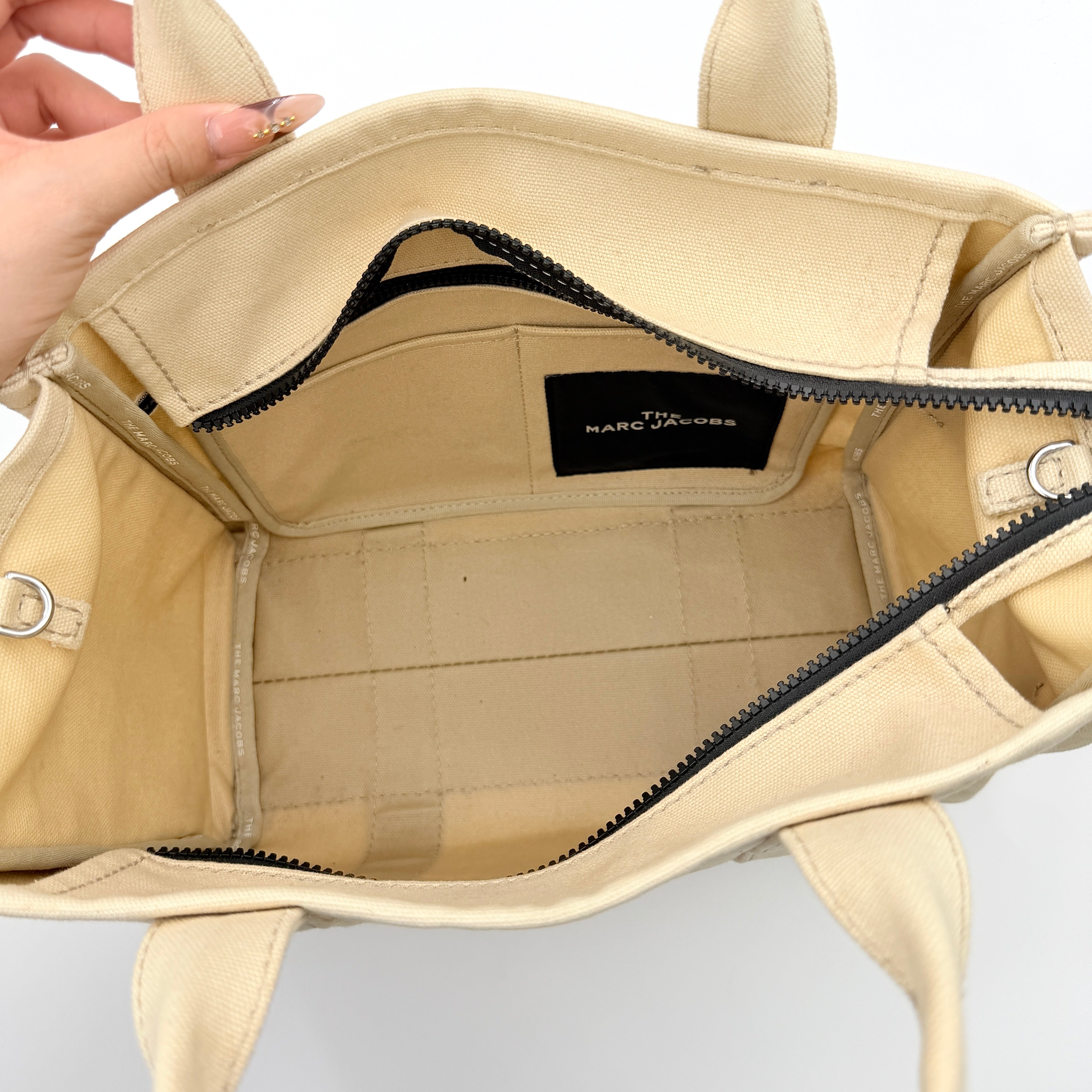 Marc Jacobs The Canvas Tote Bag in beige canvas with bold text, featuring top handles and zip closure.