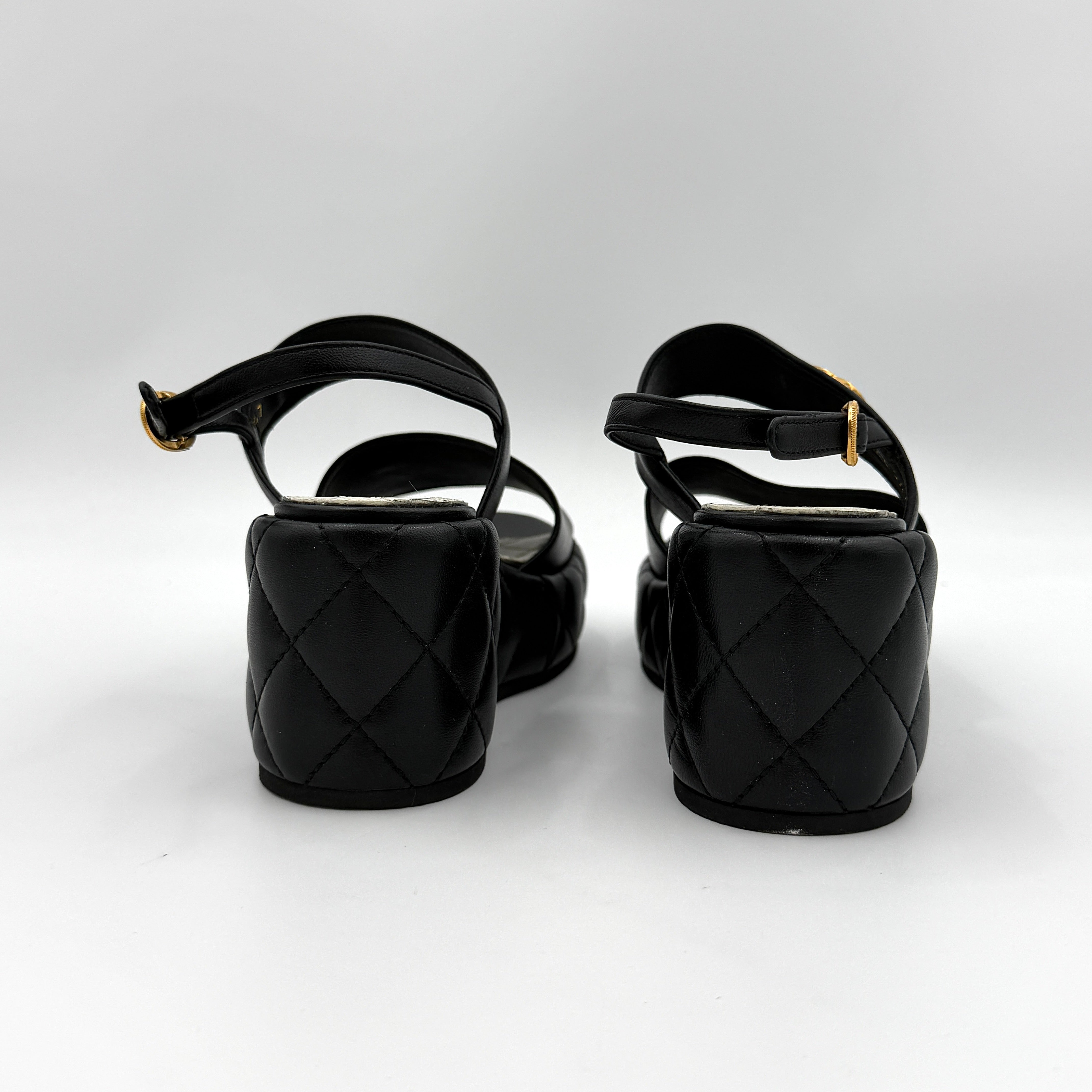 Chanel black quilted leather wedge platform sandals with gold crystal CC hardware and ankle strap detailing.