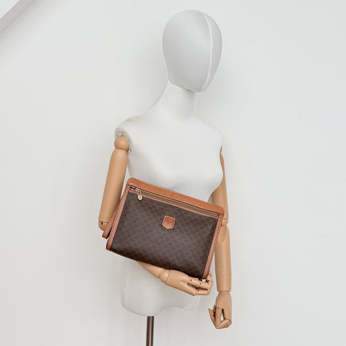 Celine Triomphe Macadam Clutch Bag in brown coated canvas with tan leather trim and gold zip, displayed against a white background.