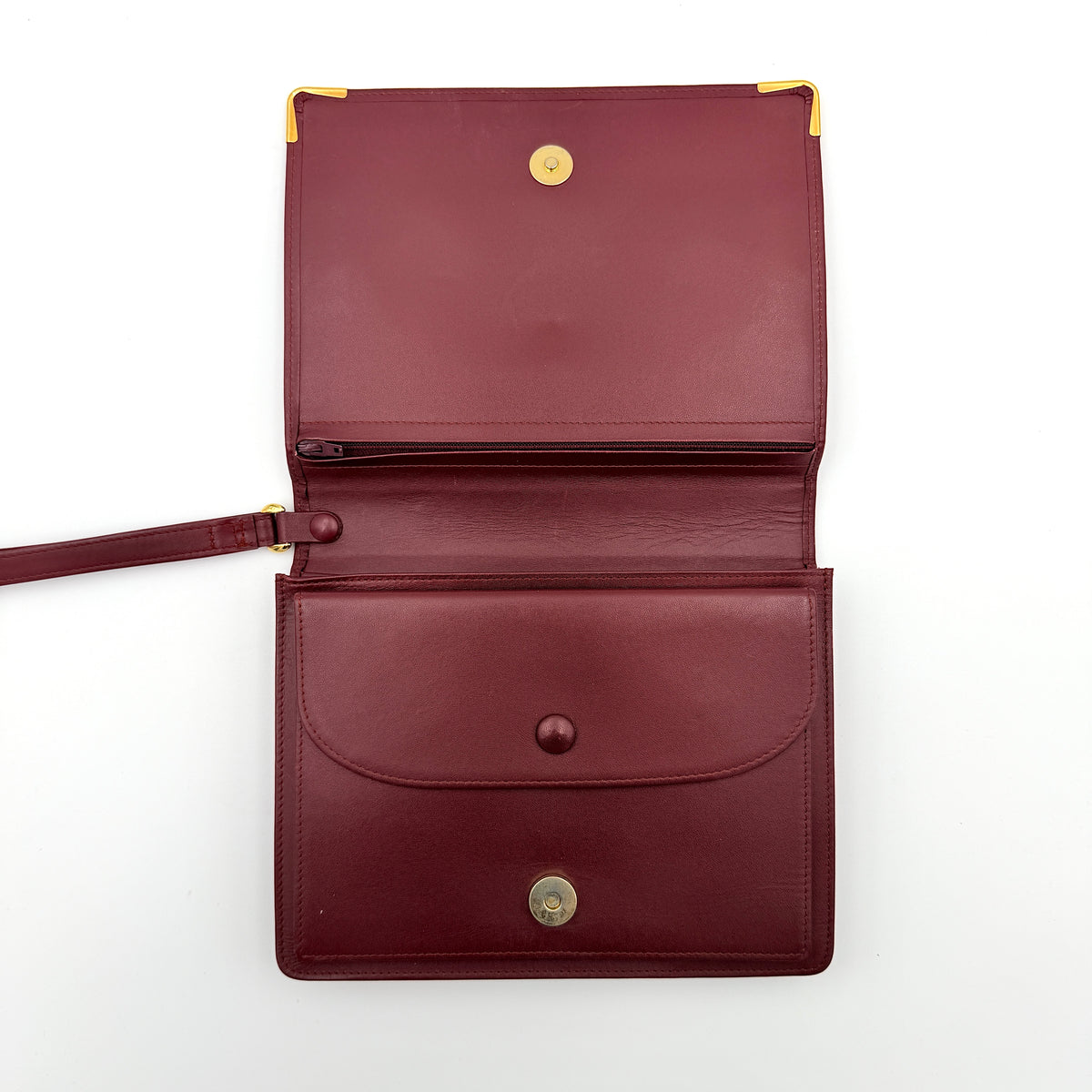 Cartier Must de Cartier wristlet clutch in burgundy leather with gold-tone corners and wrist strap, pictured with authenticity card and booklet.